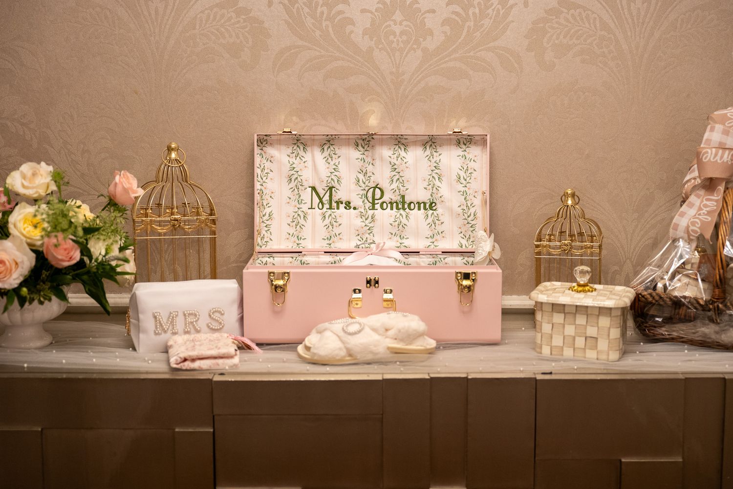 Decorative pink trunk labeled Mrs. Pontens displayed on a table with birdcage accents and floral arrangements.
