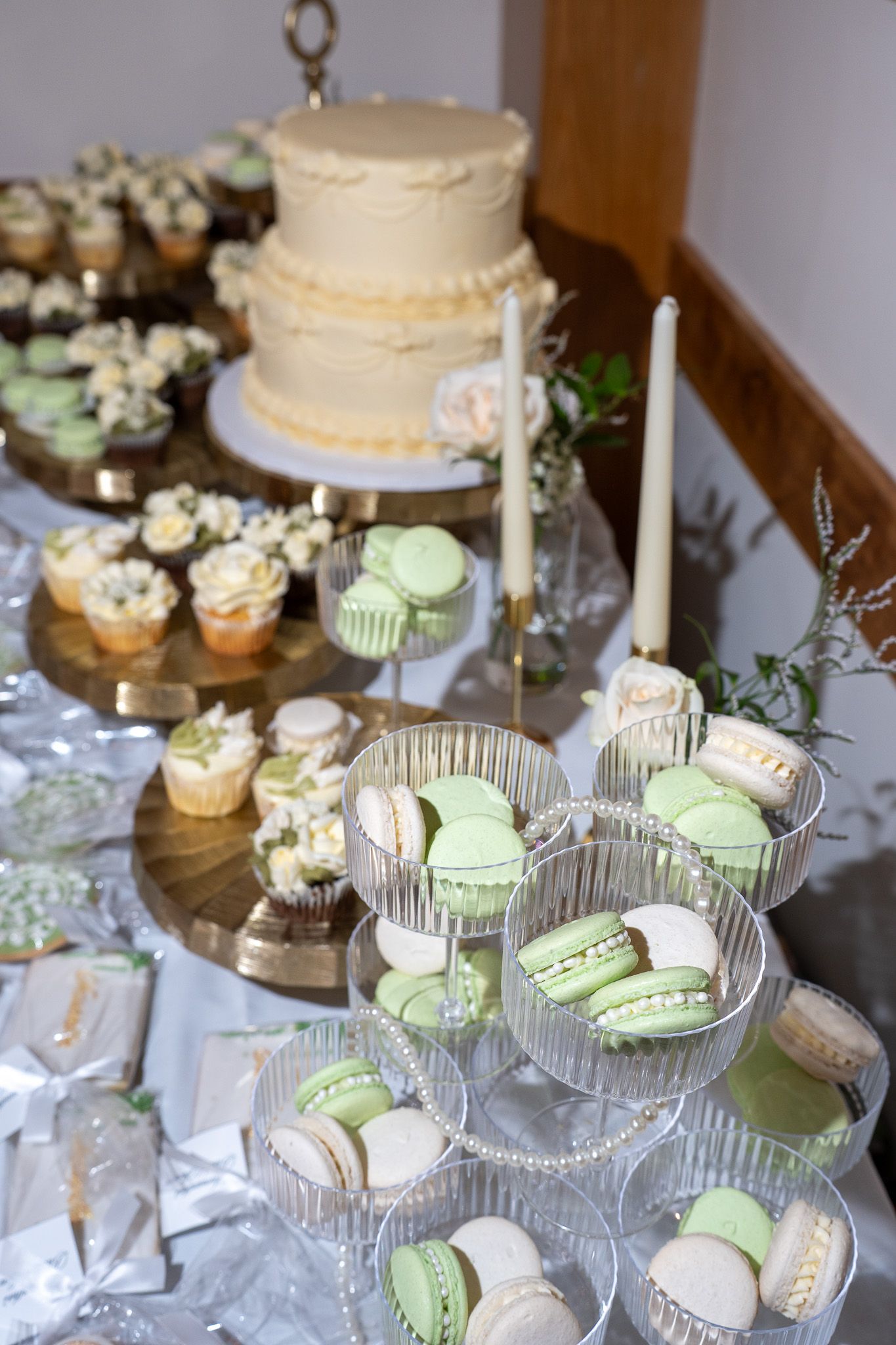 Bridal shower dessert table featuring white cake, green and white macarons, and floral cupcakes on gold stands.