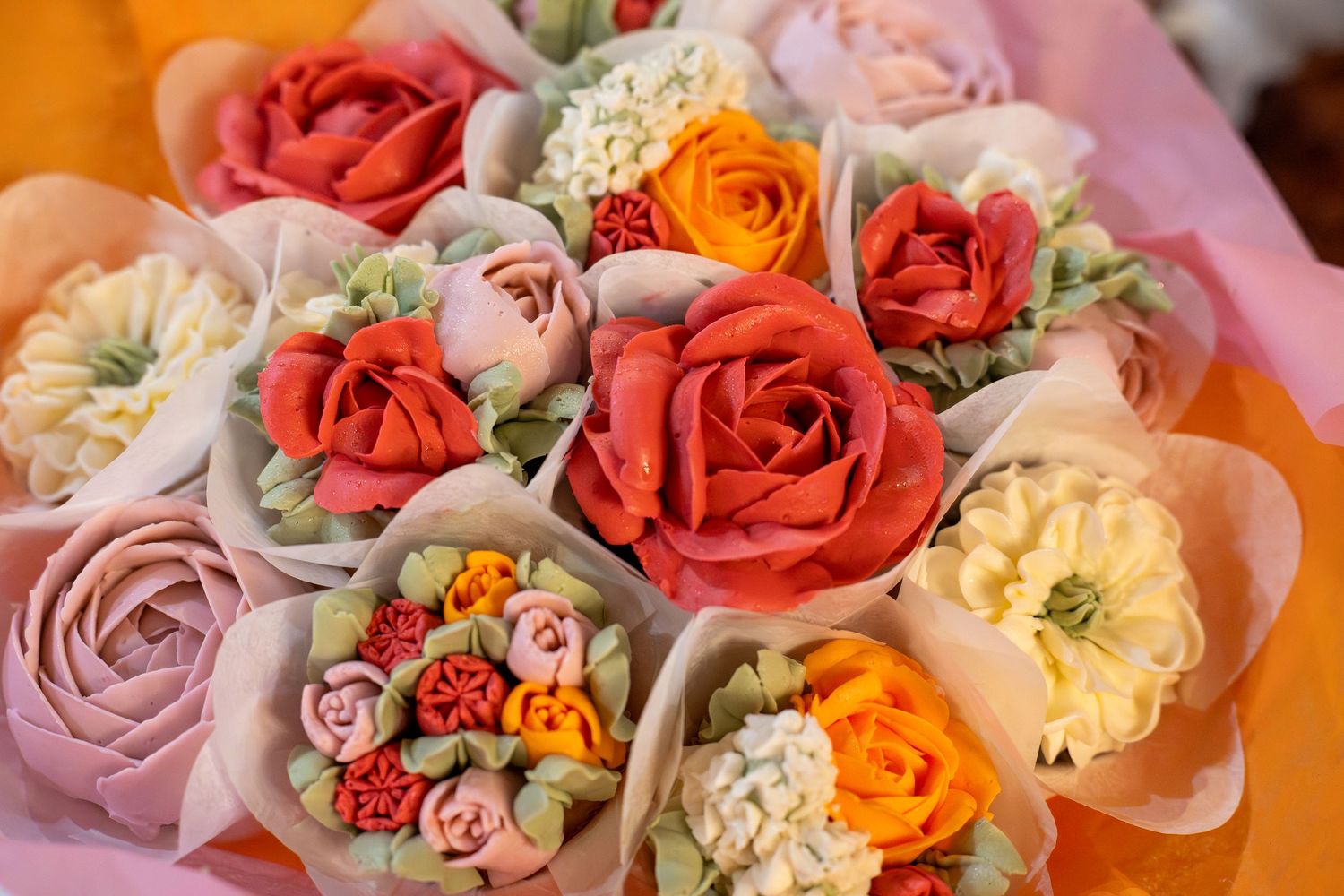 Colorful bouquet of handcrafted fondant flowers including roses in red, pink, orange, and yellow wrapped in decorative paper.