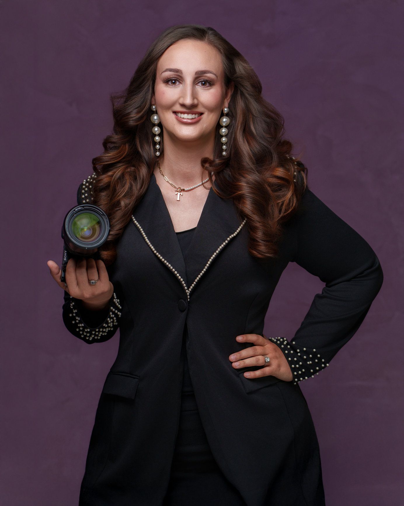 Studio portrait with person in black blazer and pearl earrings against purple backdrop.