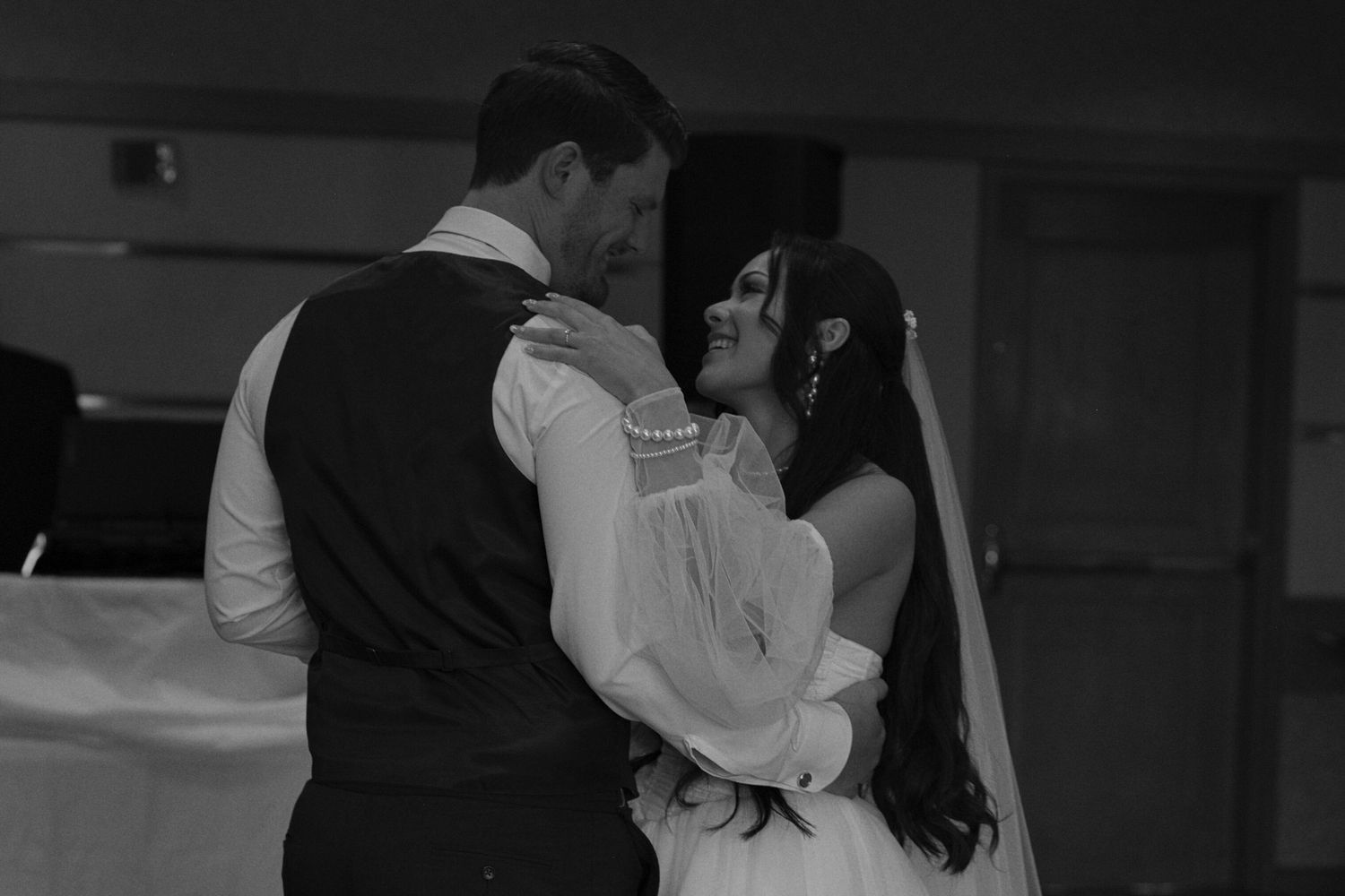Black and white photo of the bride and groom smiling at each other while they have their first dance.