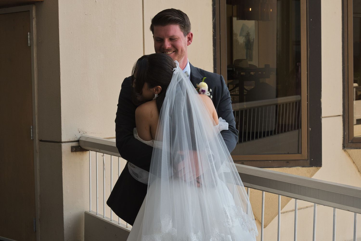 Groom hugs bride after they shared their first look together, outside on a balcony in natural light.
