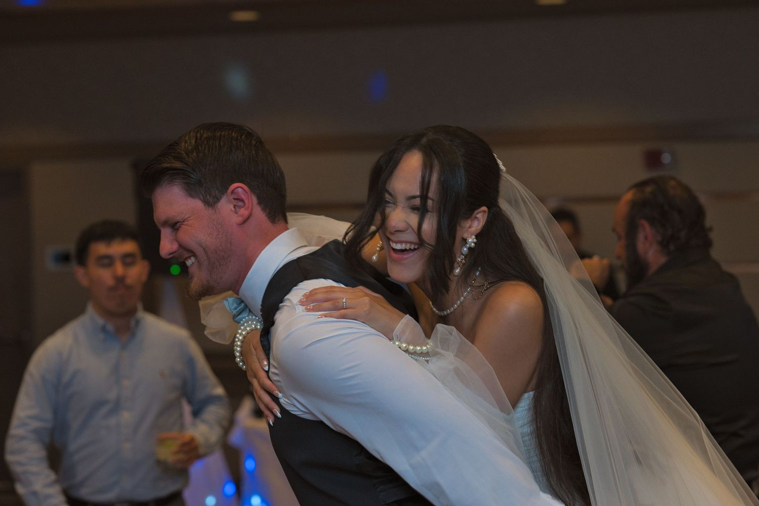 Bride and groom laugh as he lowers her off of his back while posing for a photograph together.