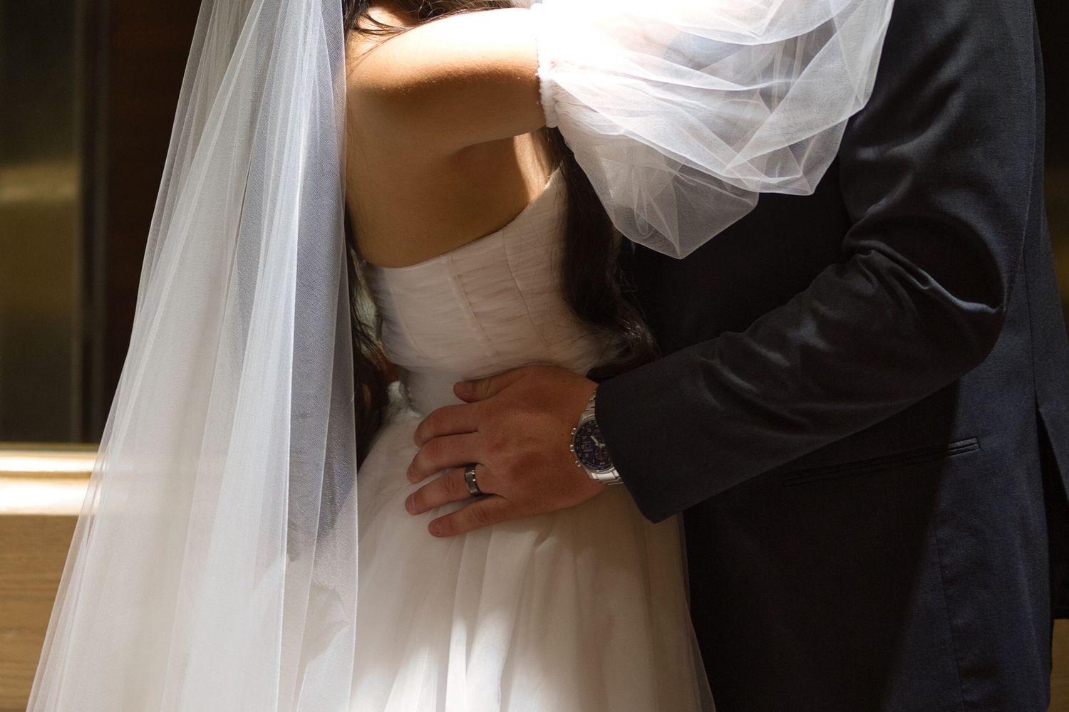 Close up of a bride and groom's embrace in an elevator, the groom's hands resting on the bride's waist.