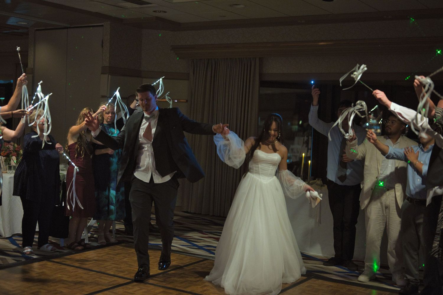 Bride and groom run between guests, cheering as they are sent off with ribbons and lights.