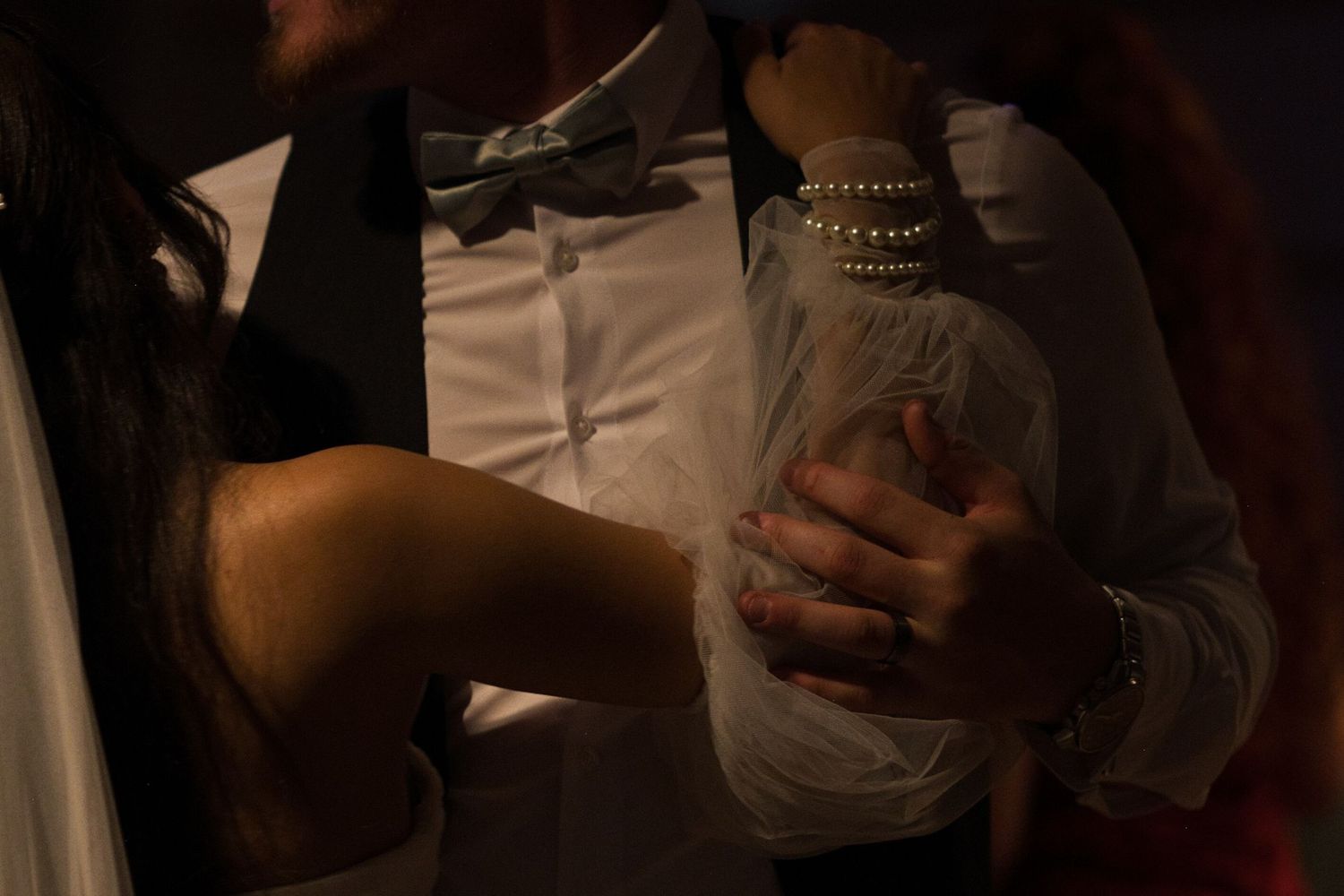 A close up shot of the groom holding his bride's arm, covered with a puffy tulle sleeve and pearl bracelets.