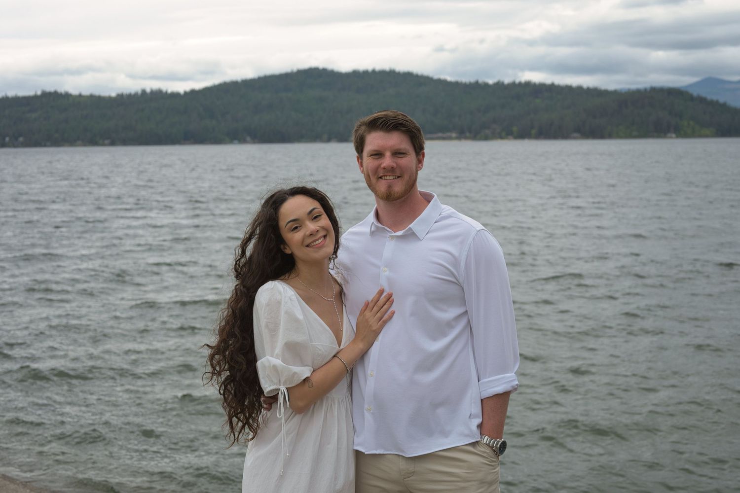 Engaged couple smile in front of Lake Coeur d' Alene