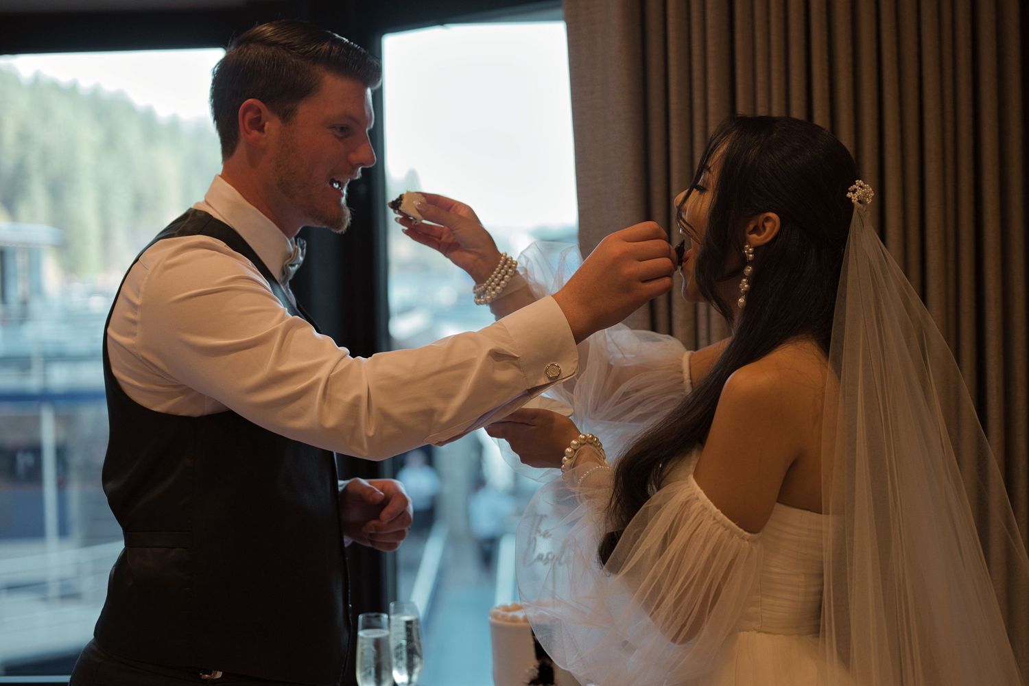 Bride and groom feed each other a bite of cake from their hands during the wedding cake cutting.