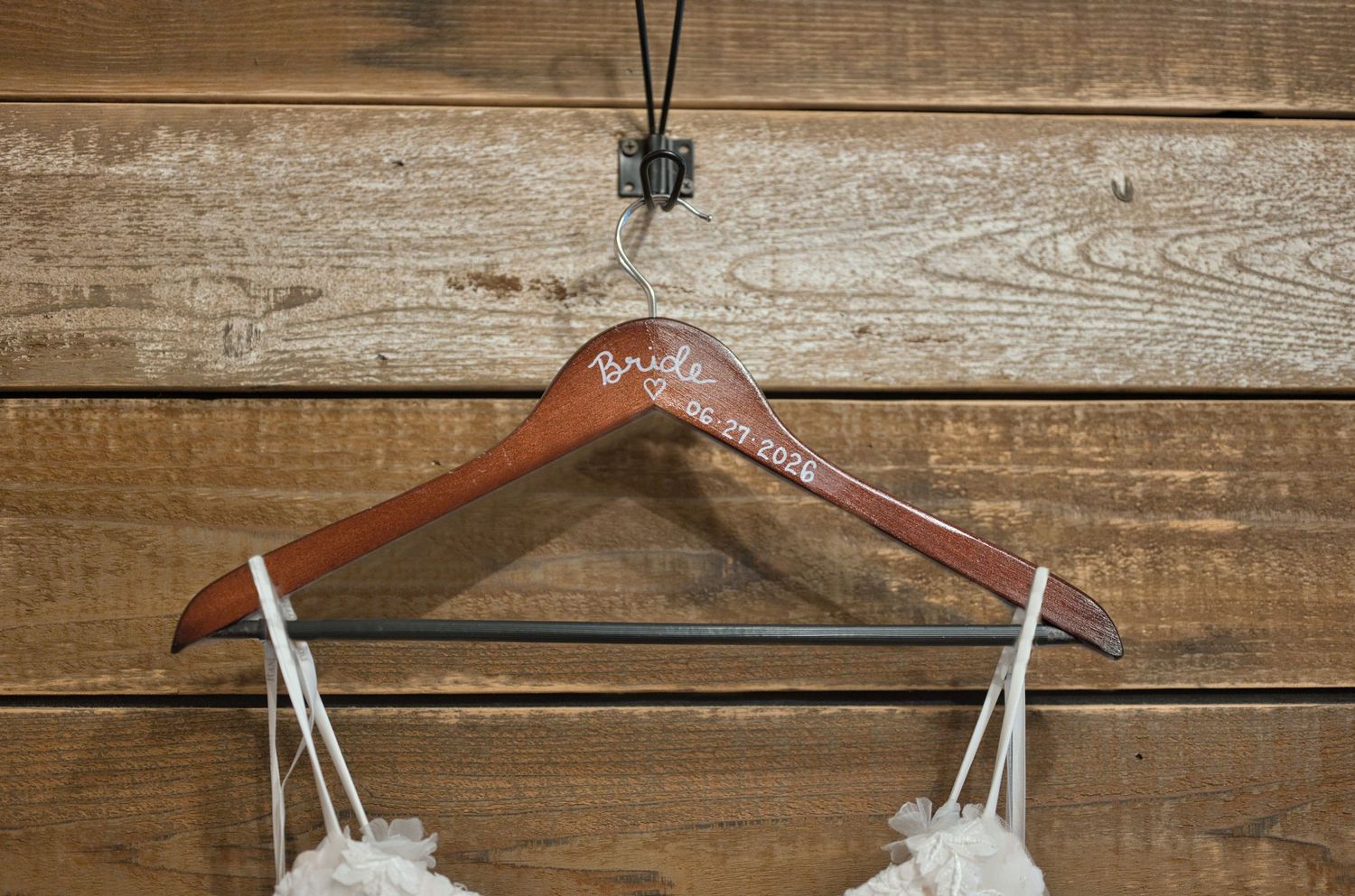 Close up of a wedding dress on a custom hanger with the wedding date hanging in front of a wooden wall.