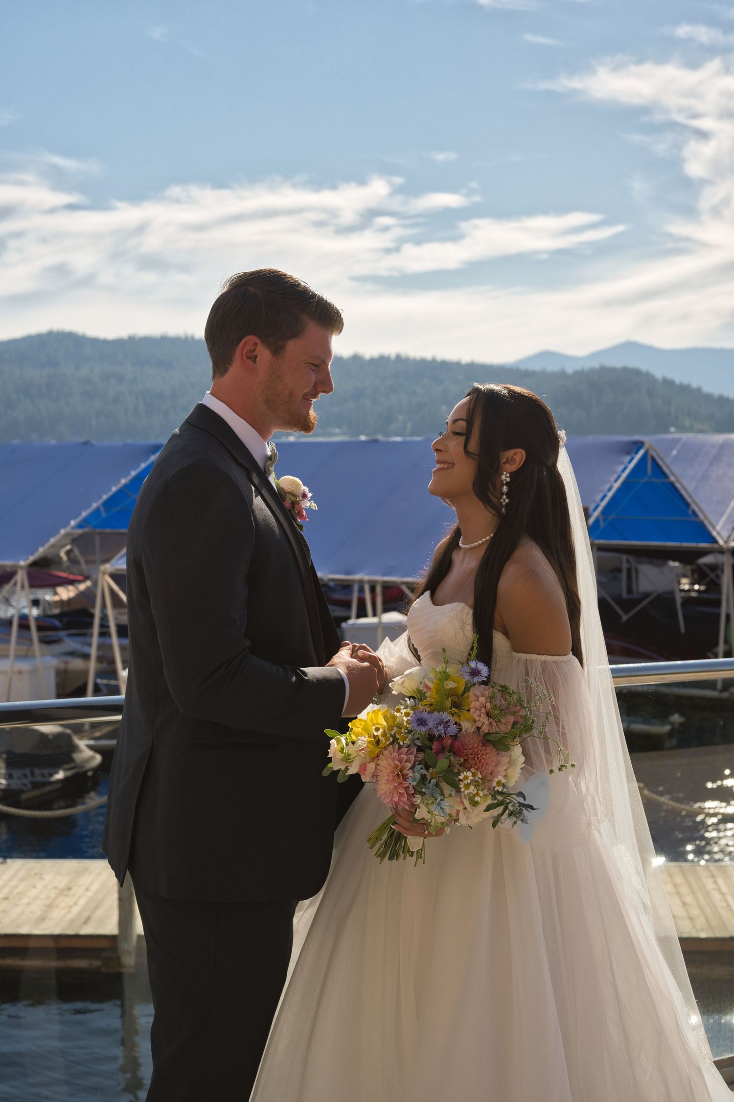 Vertical picture of bride and groom's profiles as they hold hands, standing outside in the sun of Coeur d' Alene.