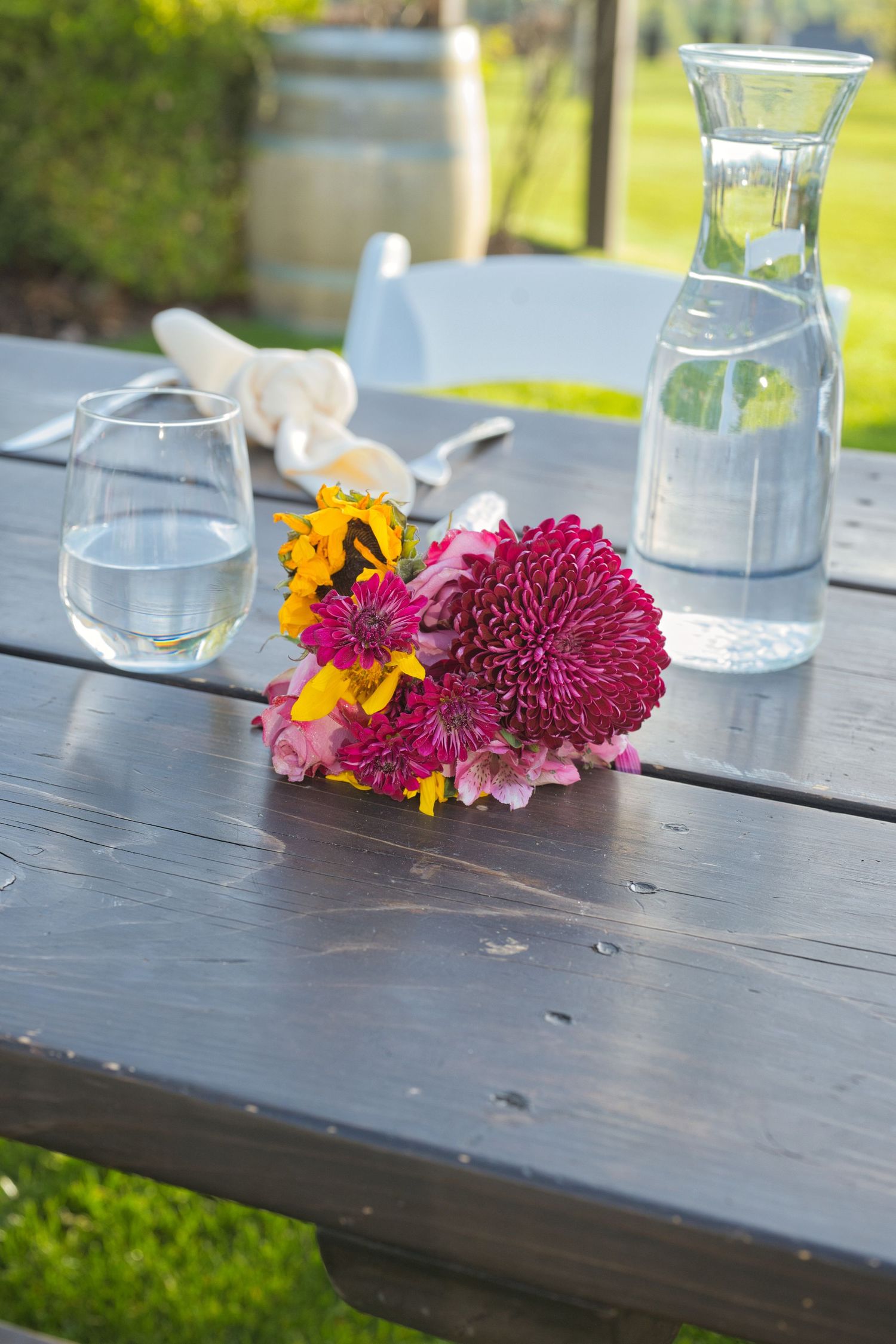 Bride's simple bouquet lays on a table with water glasses next to it, the flowers a vibrant magenta and yellow in Eastern Washington wedding