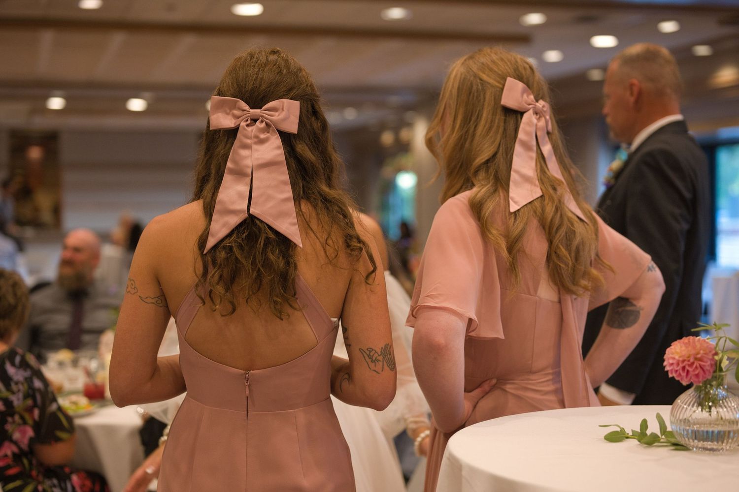 Focus on pink bows in the bridesmaids hair as they look on towards the guests during reception.