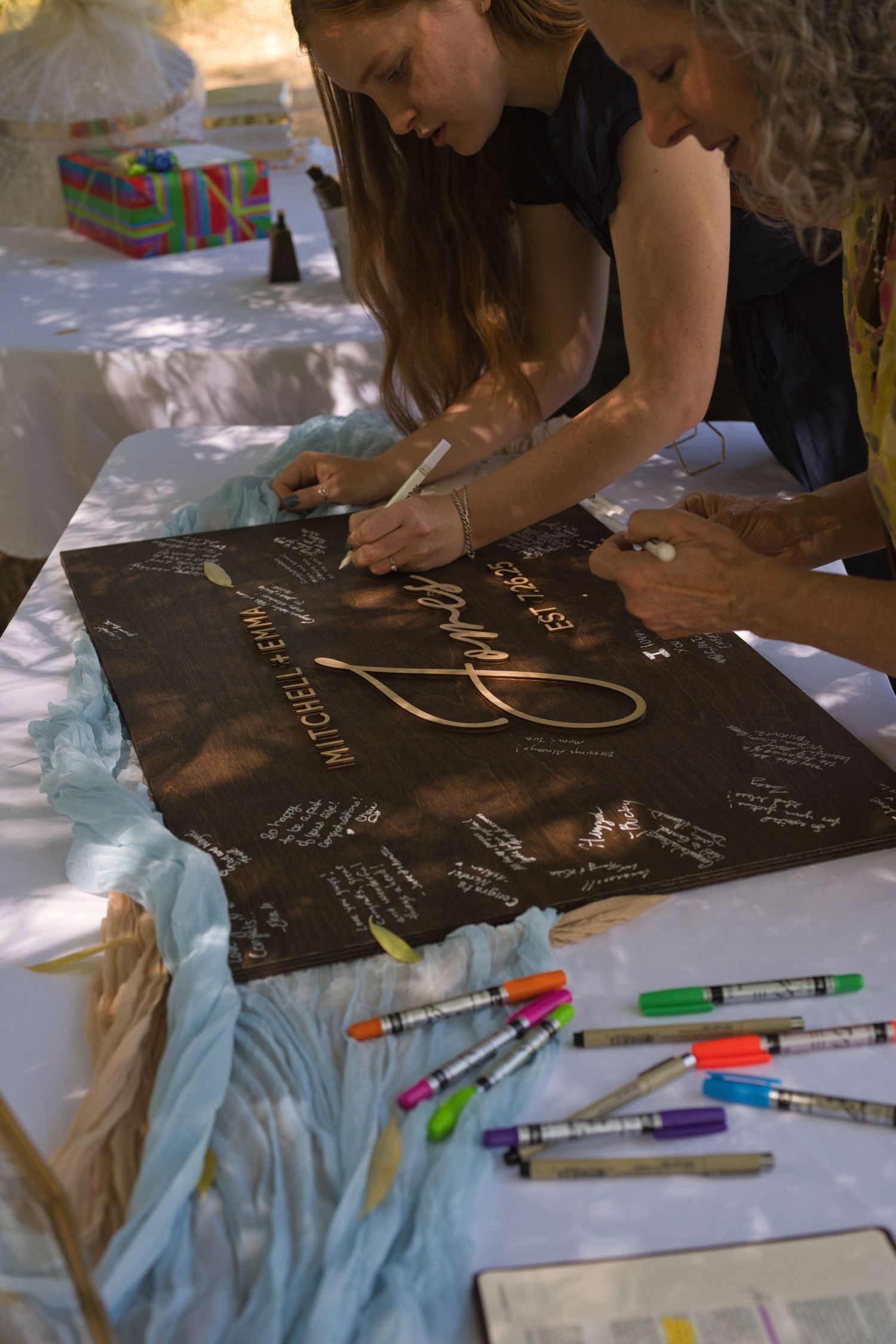 Guests writing on a sign that features the couples names and wedding date, serving as their guestbook.