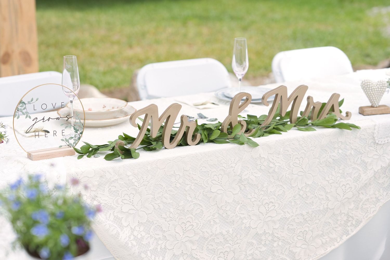 Mr. and Mrs. Sign on the bride and groom's head table for reception, a white cloth and greenery around it.
