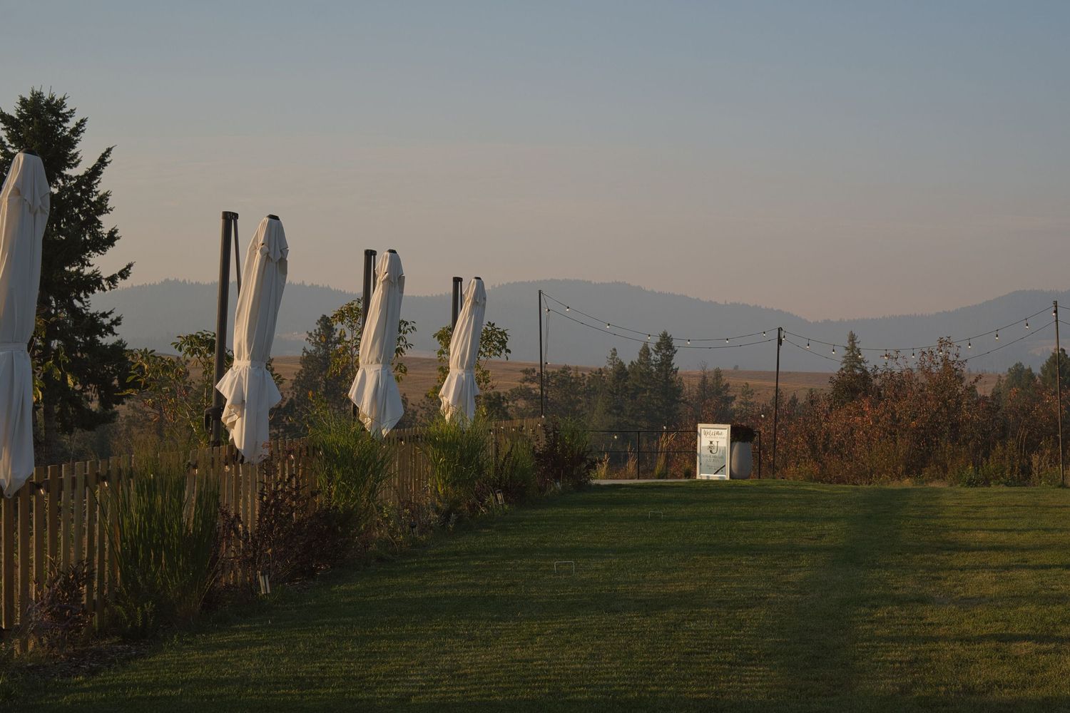 Moody picture of greenhouse venue lawn as the sun sets in Rockford, Washington, mountains rising in the far distance.
