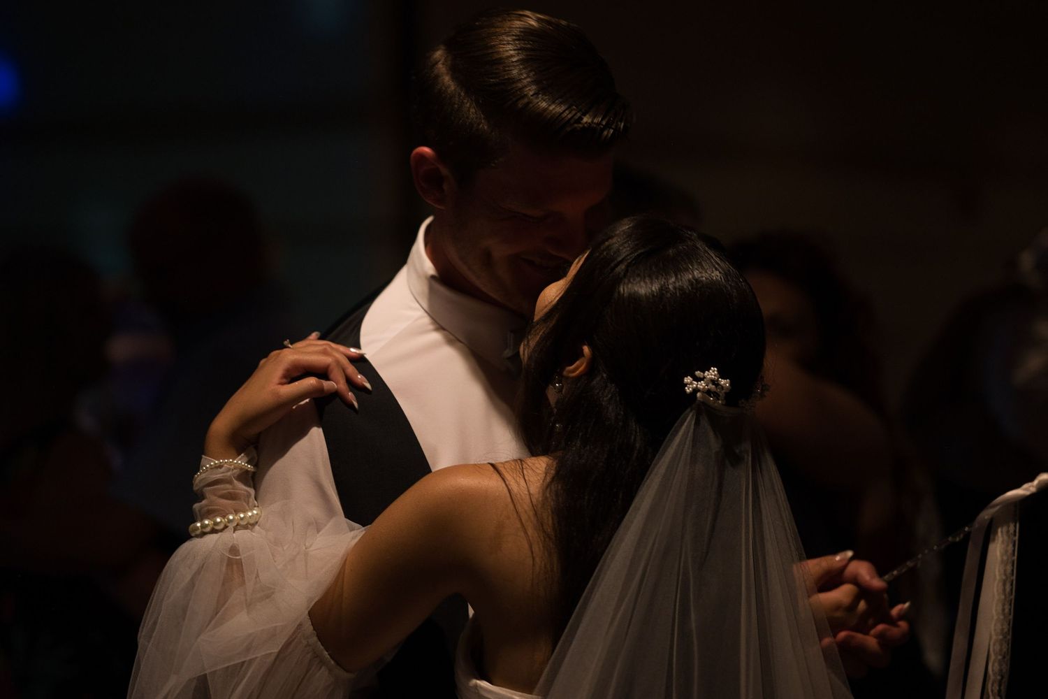 Bride and groom dancing together under a dramatic light, holding each other closely.