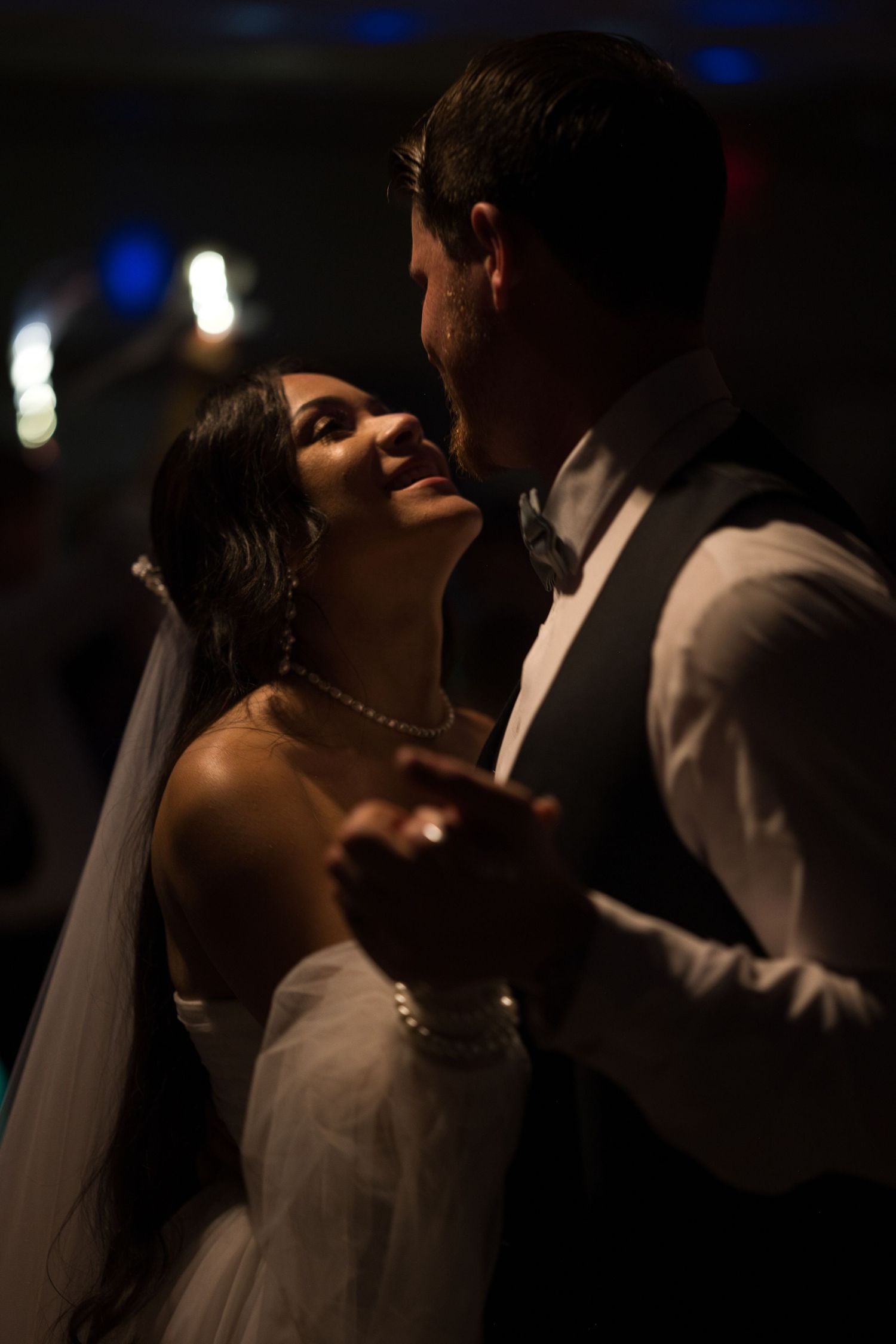 Bride and groom smile at each other while holding each others hands as they dance together.