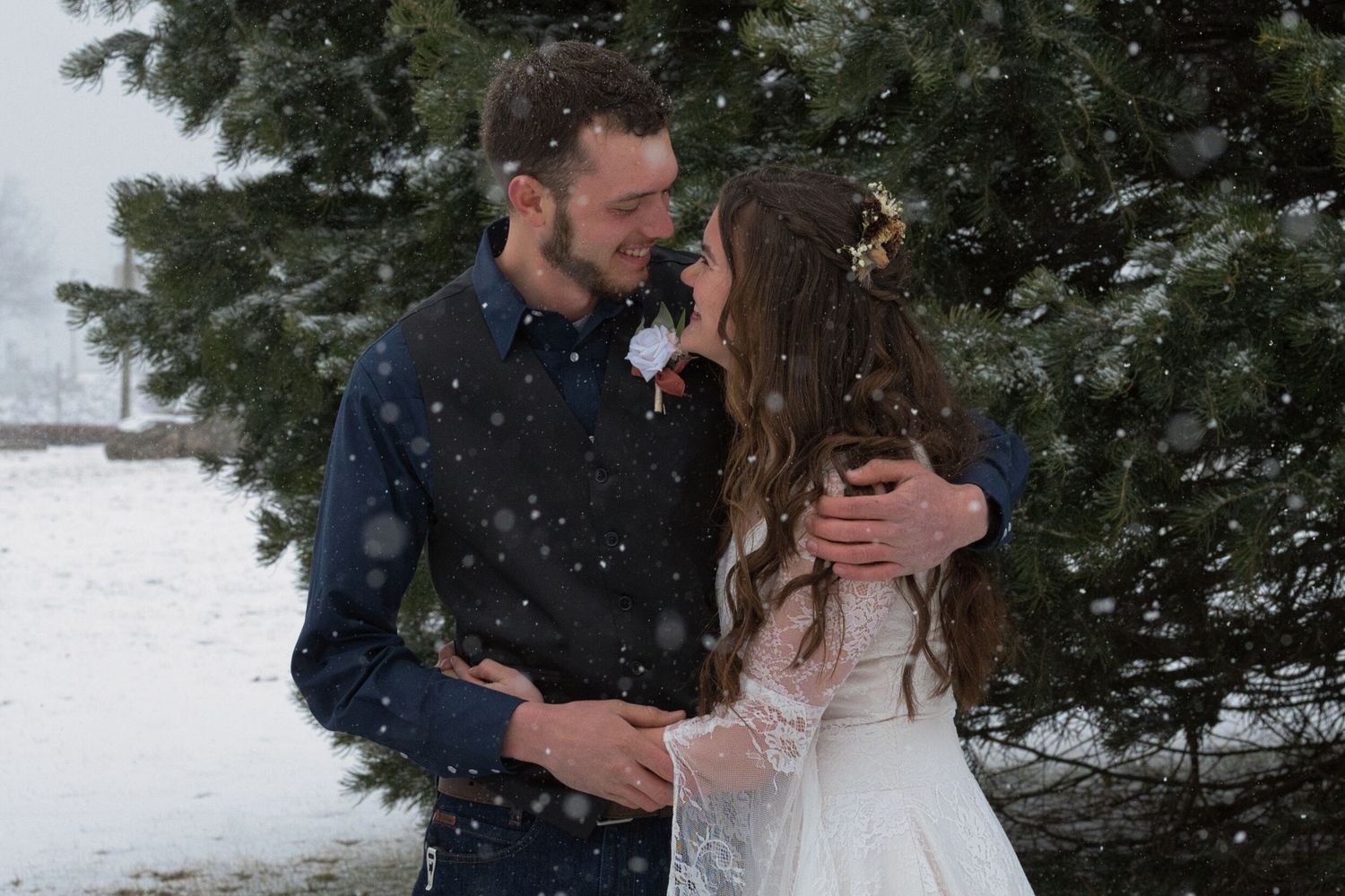 Bride and groom laughing and smiling at each other as they stand in the snowy trees in Sandpoint, Idaho before their wedding.