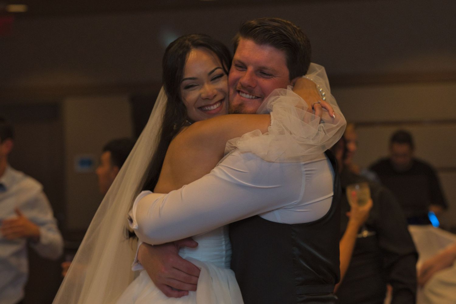 Bride and groom press faces together while hugging each other tightly as they pose for a photo taken by a friend.