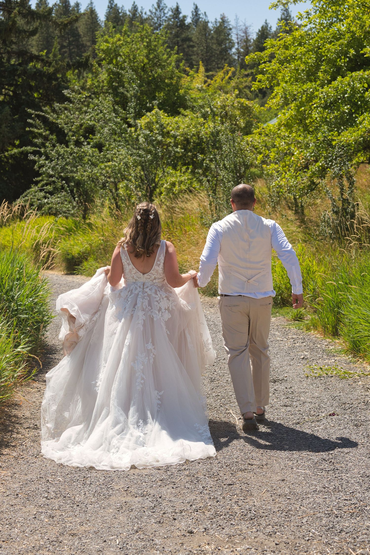 Bride and groom walk away down a gravel road, the bride's dress billowing behind her.