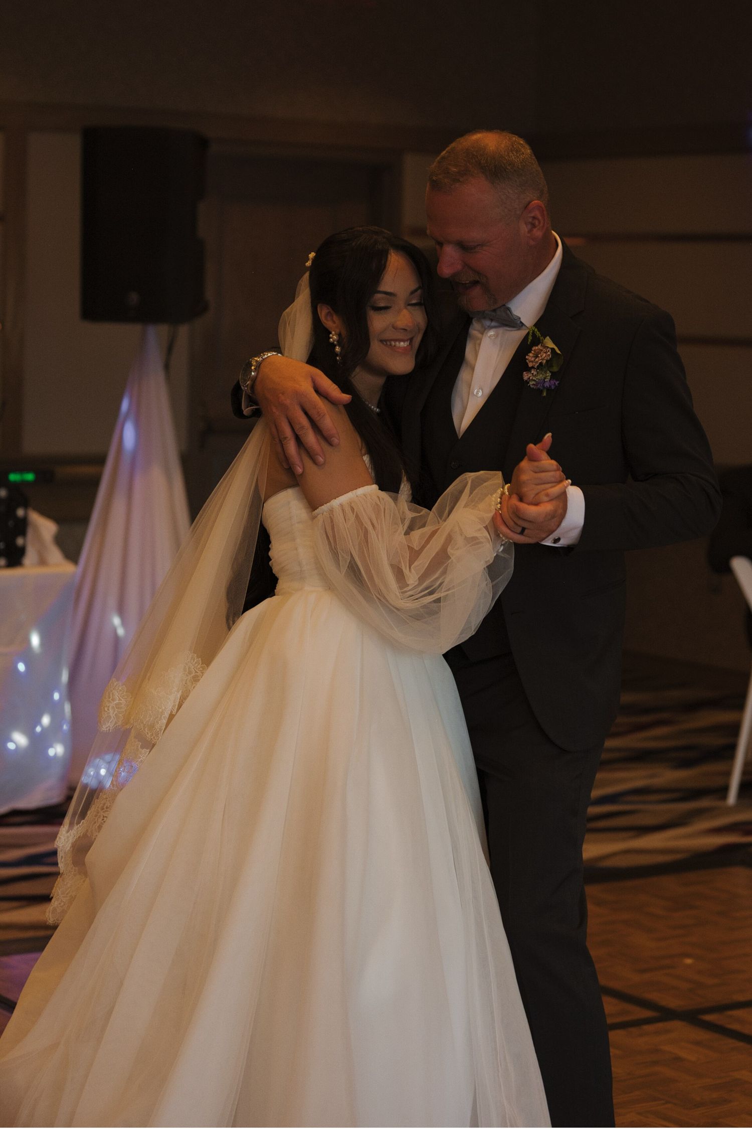 Bride dancing with her father during the father-daughter dance, he hugs her close to him with his arm around her shoulders.