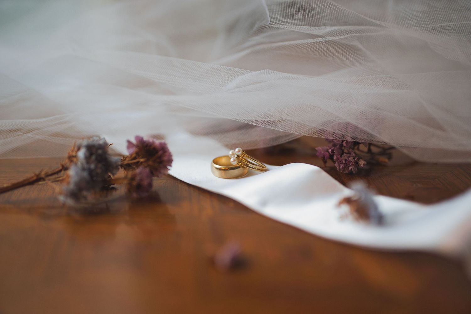 Detail pictures of wedding bands arranged on a ribbon with flowers and a veil draped across the rings.