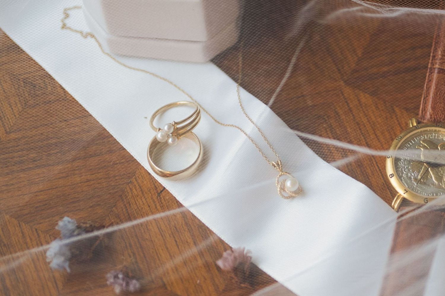 Wedding detail flat lay featuring wedding rings, necklace, and a watch, with a veil draped across the top.