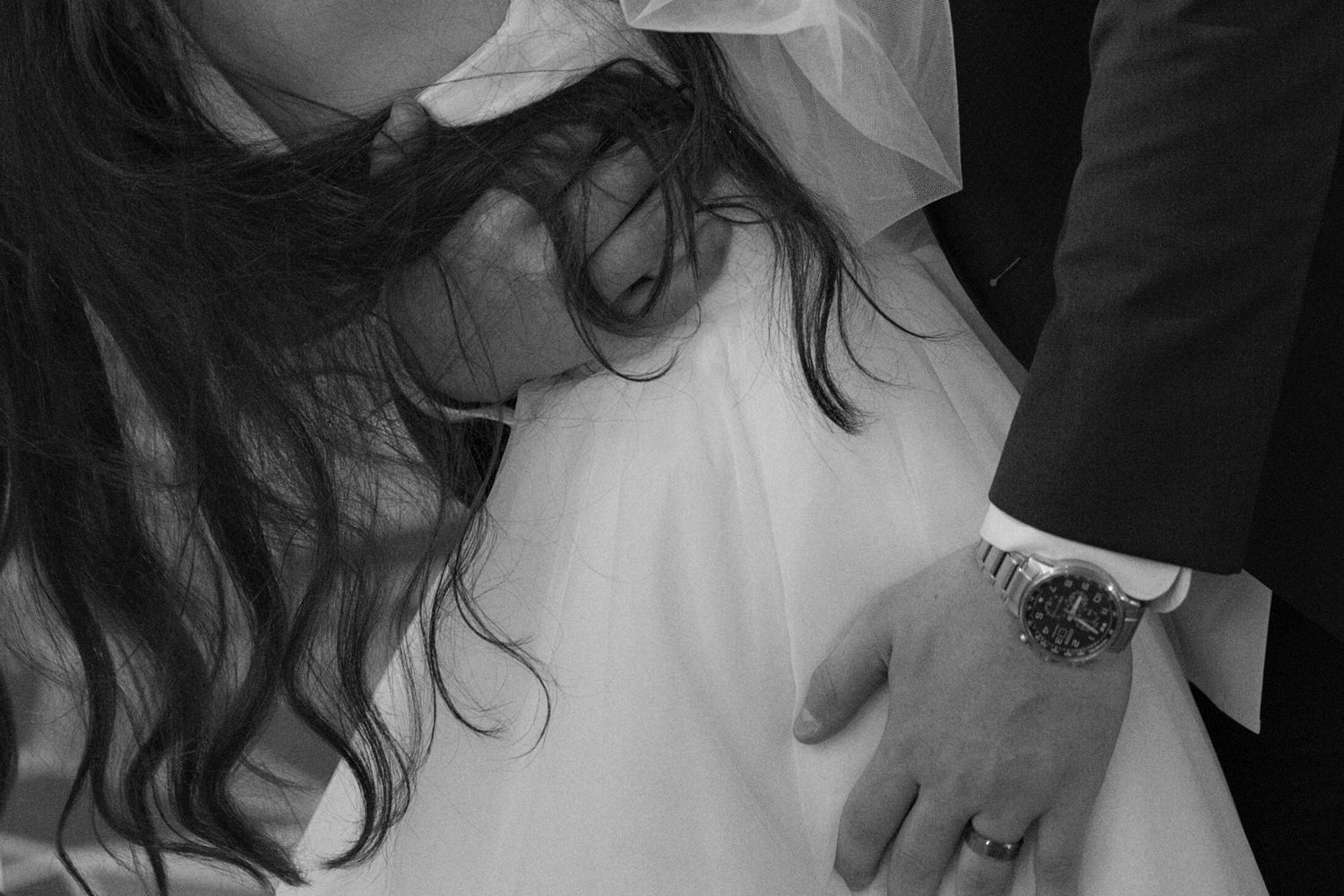 Close up black and white photograph focusing on the groom's hands as he pulls the bride closer to him.