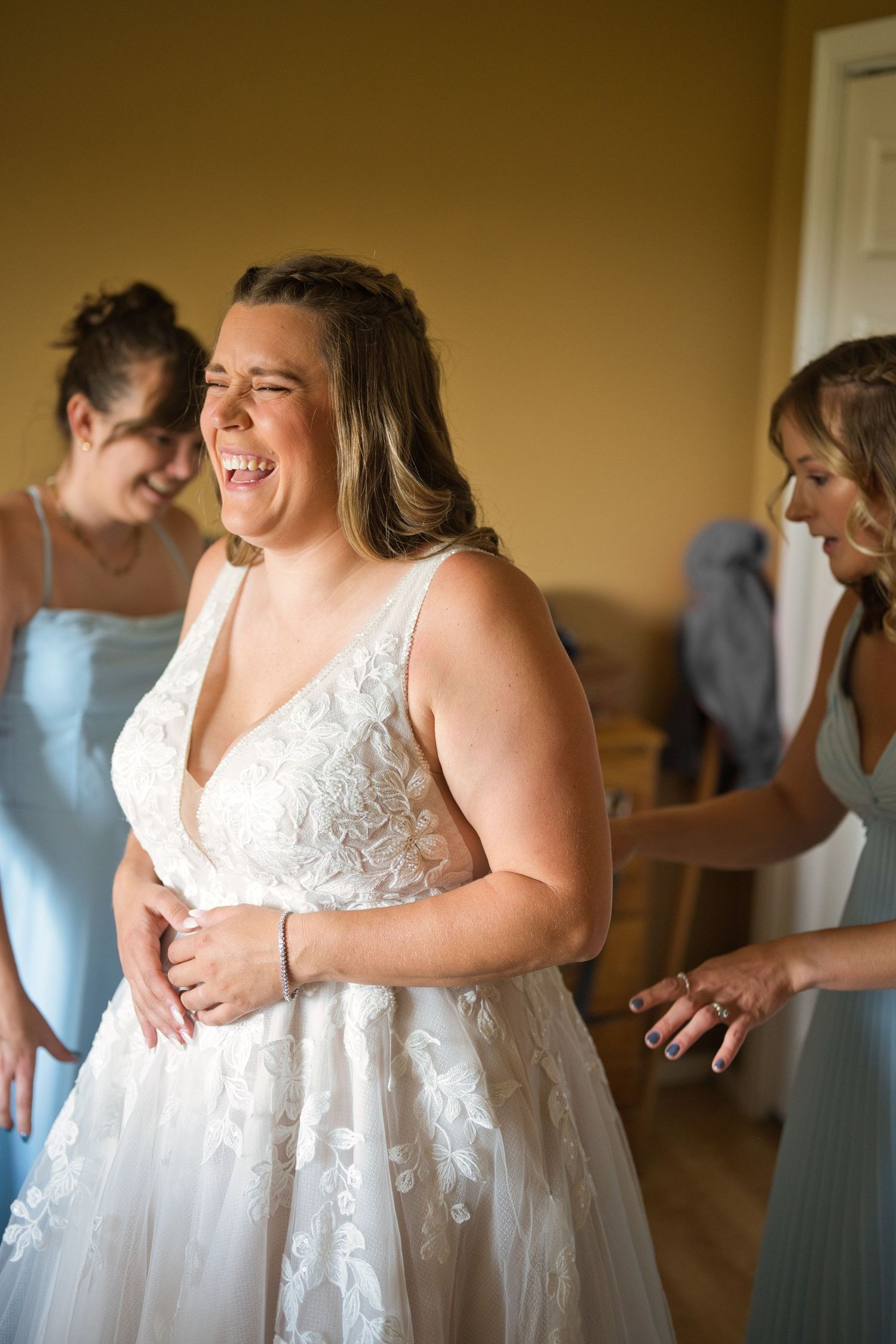 Candid moment of bride laughing while bridesmaids fix her dress