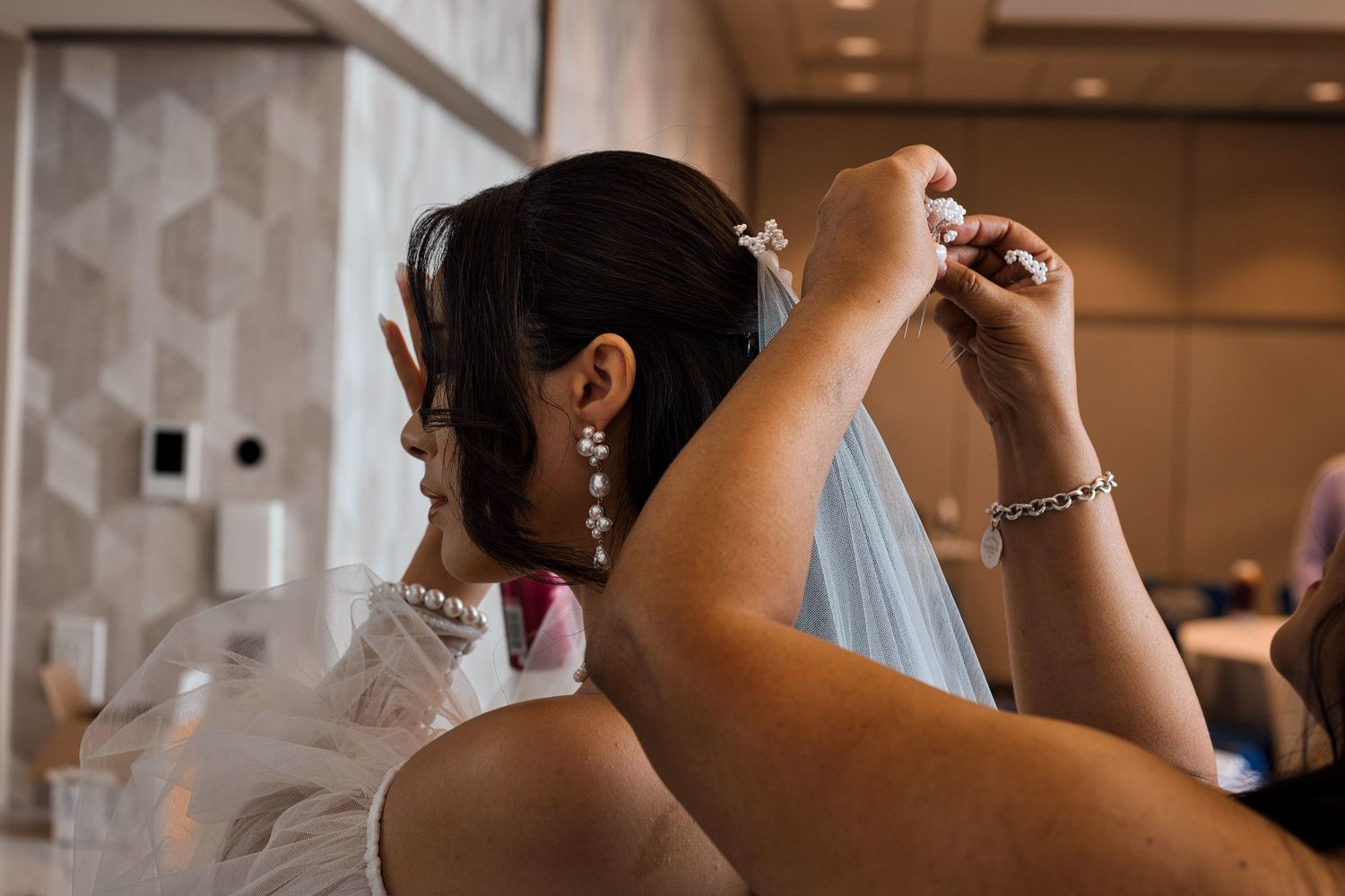 Mother of the bride attaching the veil into the bride's hair while the bride arranges her hair.