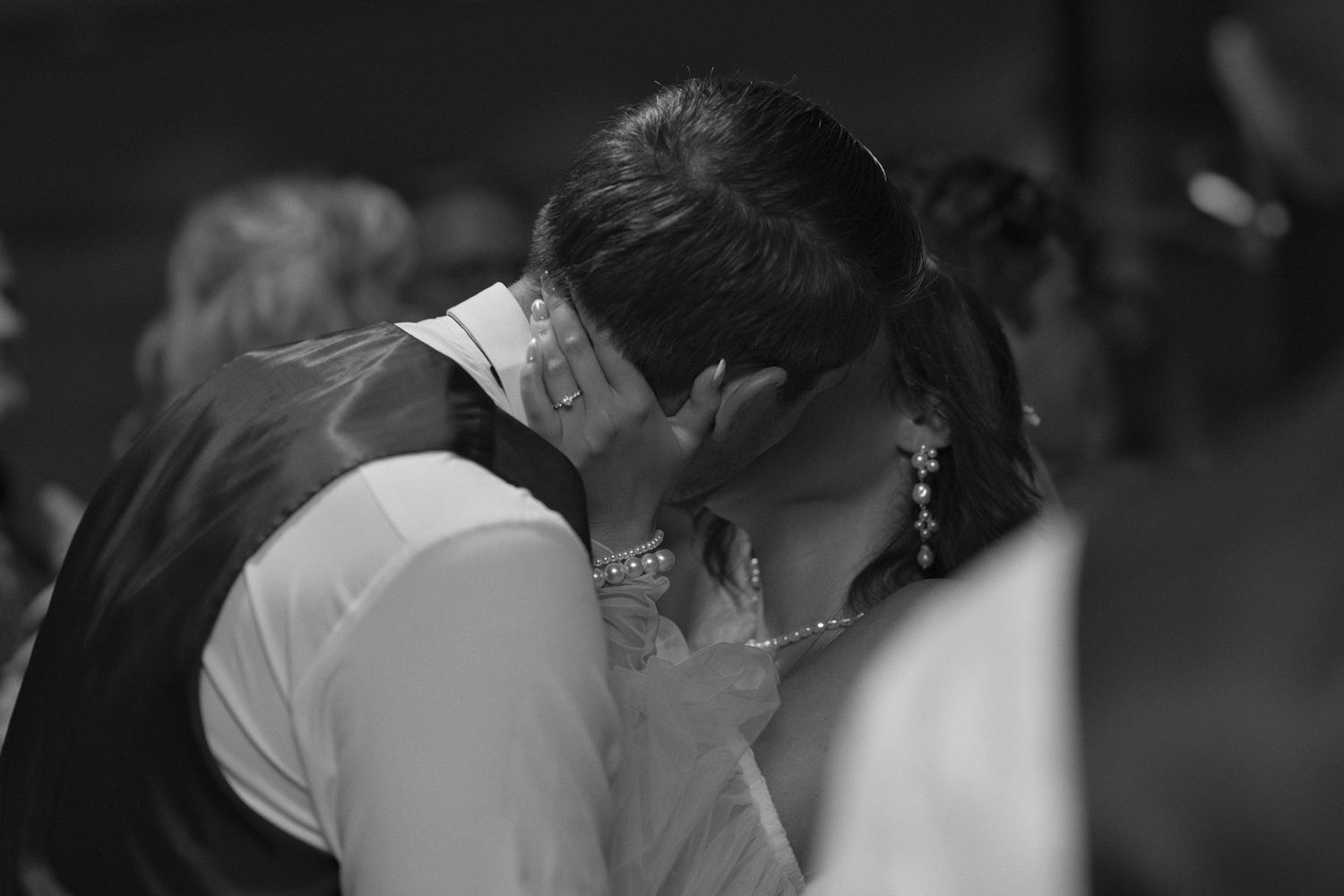 Black and white photo of bride and groom kissing, with the bride's hand on the grooms neck, pulling him closer.