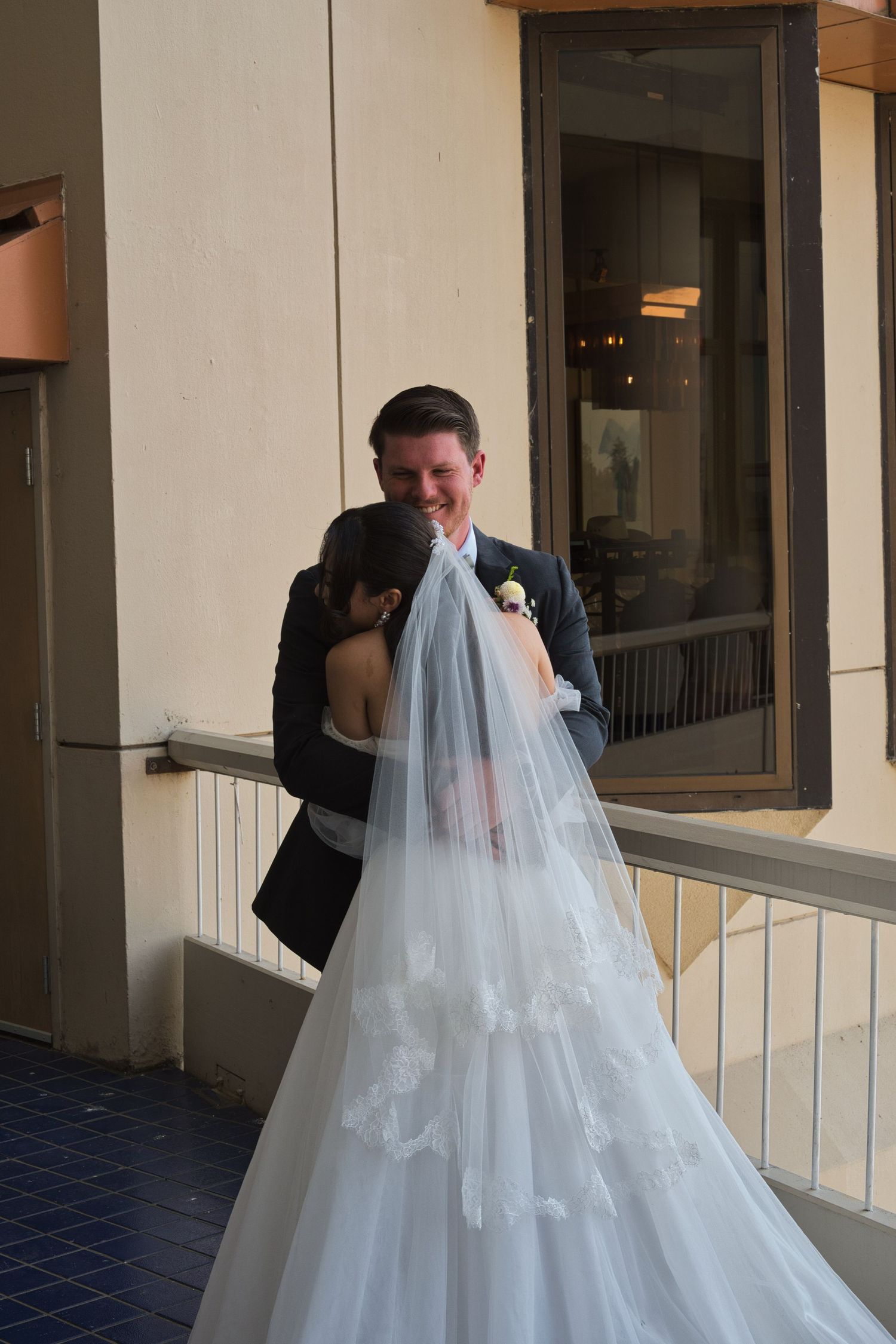 Groom hugs his bride as they embrace after their first look, while the picture highlights the bride's veil and dress.