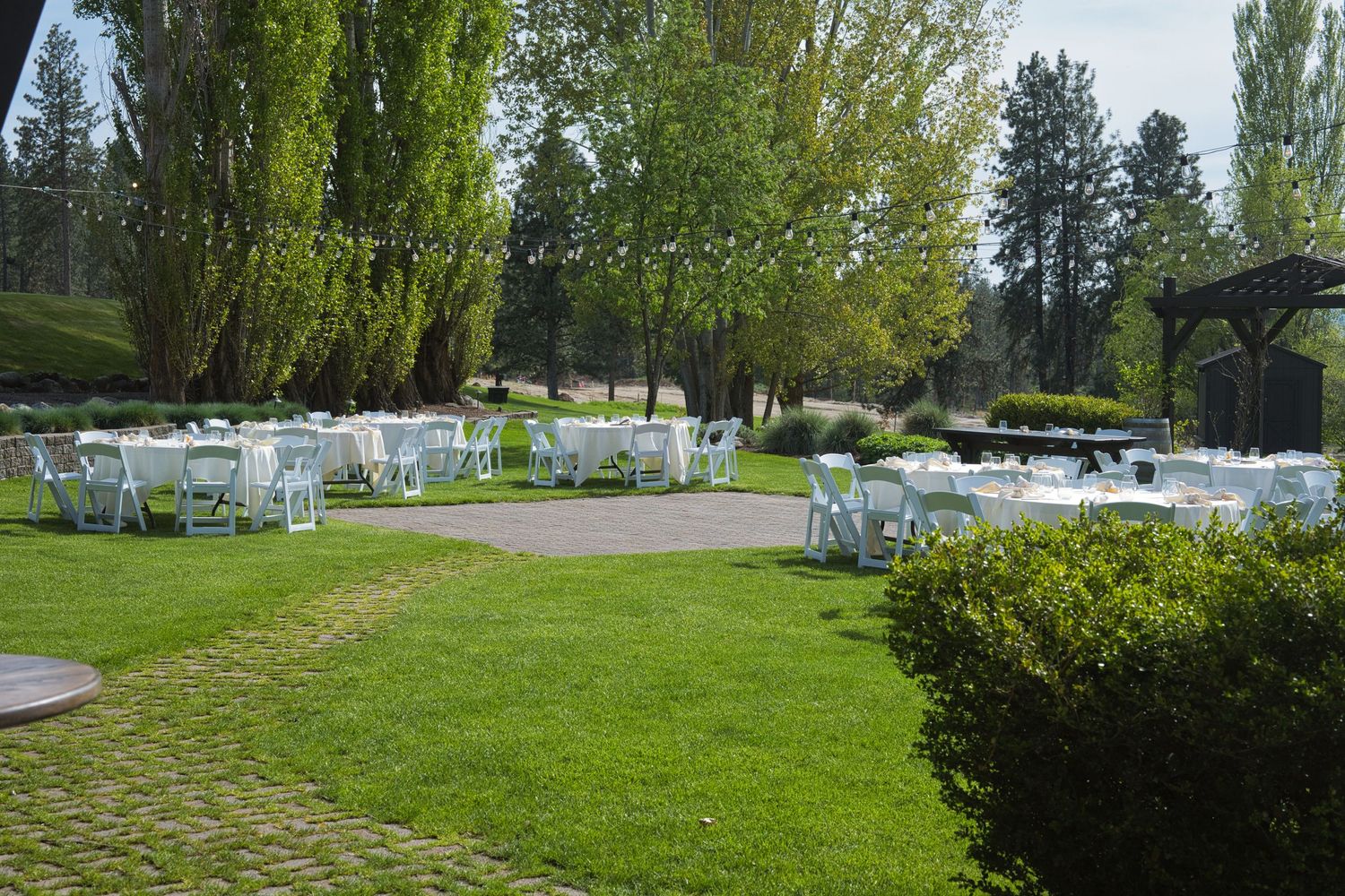 Wide shot of the Beacon Hill Weddings and Events venue in Spokane, Washington, set up with white tables and lights strung across the patio.