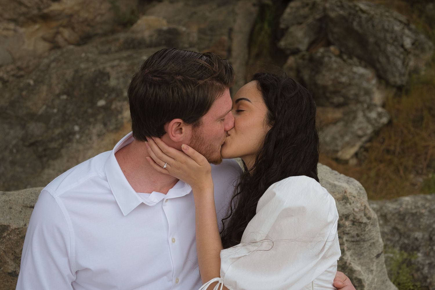 Engaged couple kiss as she places her hand on his face