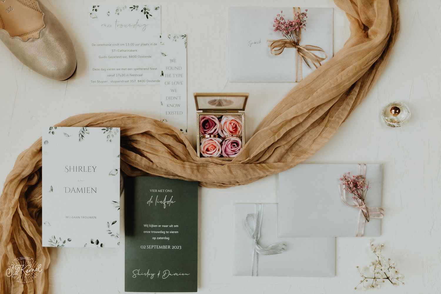 Romantische flatlay van trouwdetails met bloemen, uitnodigingen en juwelen – gefotografeerd in Brugge en West-Vlaanderen.