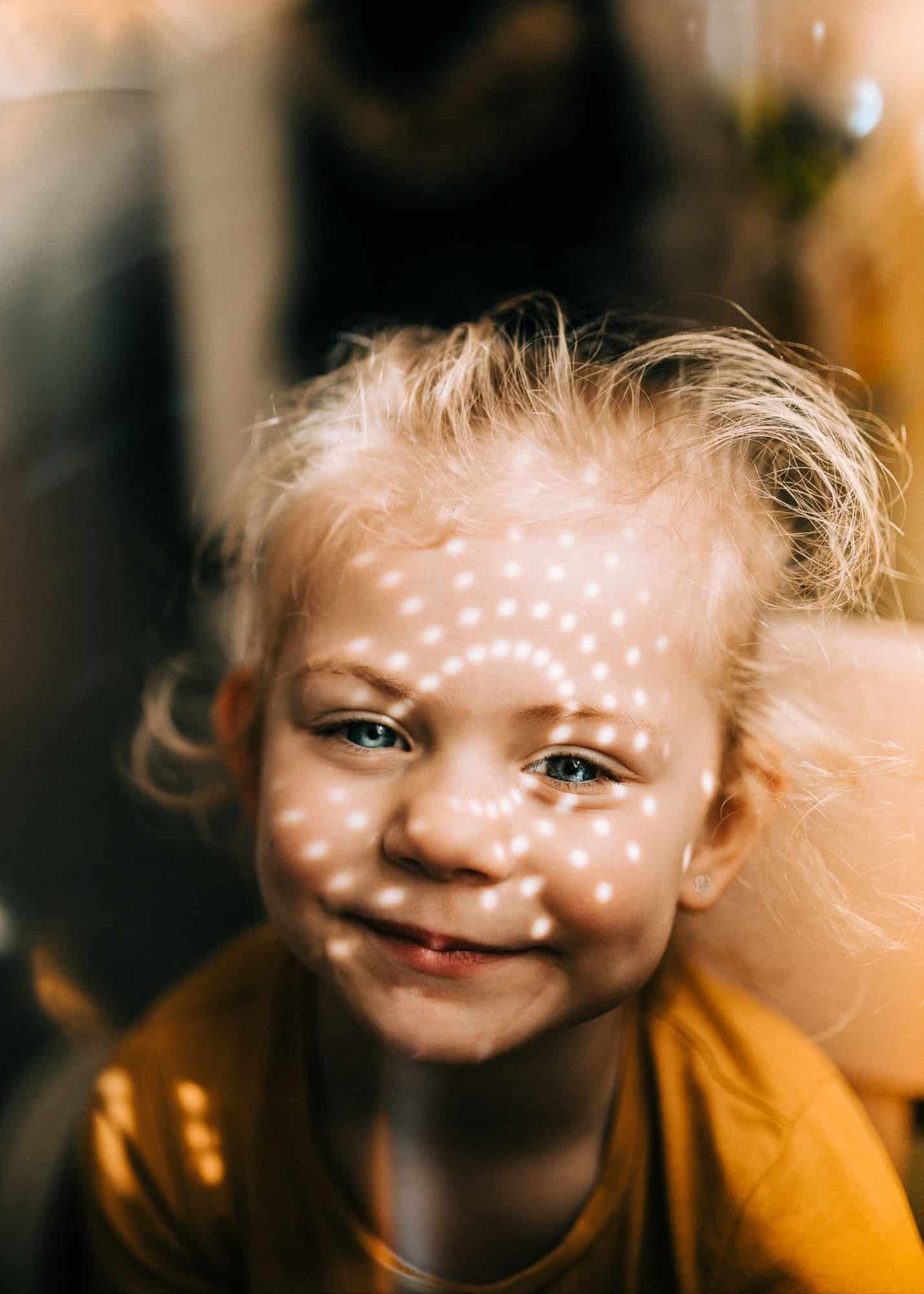 Een lachend kind met krullen wordt verlicht door zonlicht met patronen tijdens een gezin fotoshoot