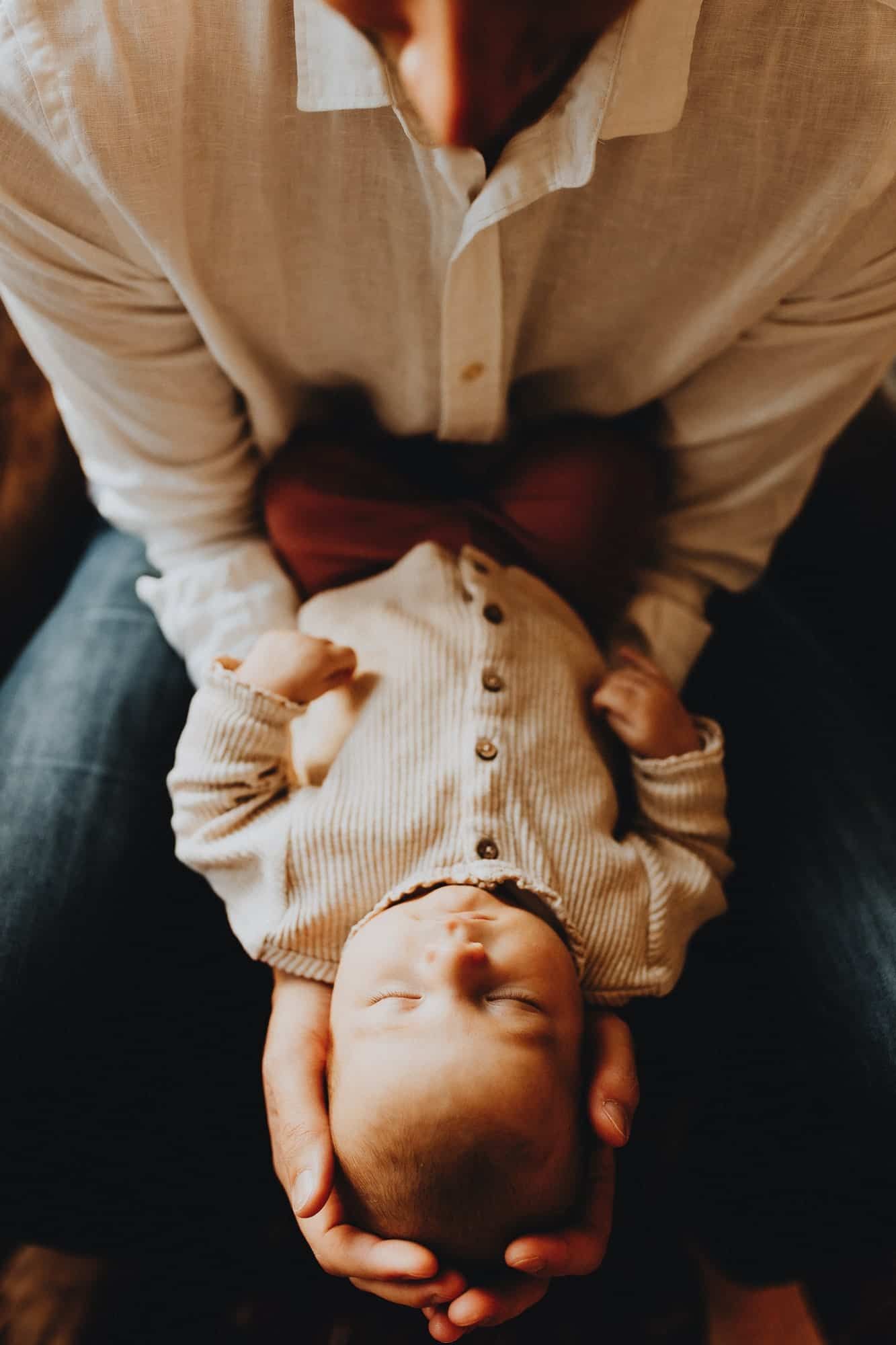 Vader houdt slapende newborn in zijn armen tijdens een warme lifestyle fotoshoot in Kortemark, West-Vlaanderen.