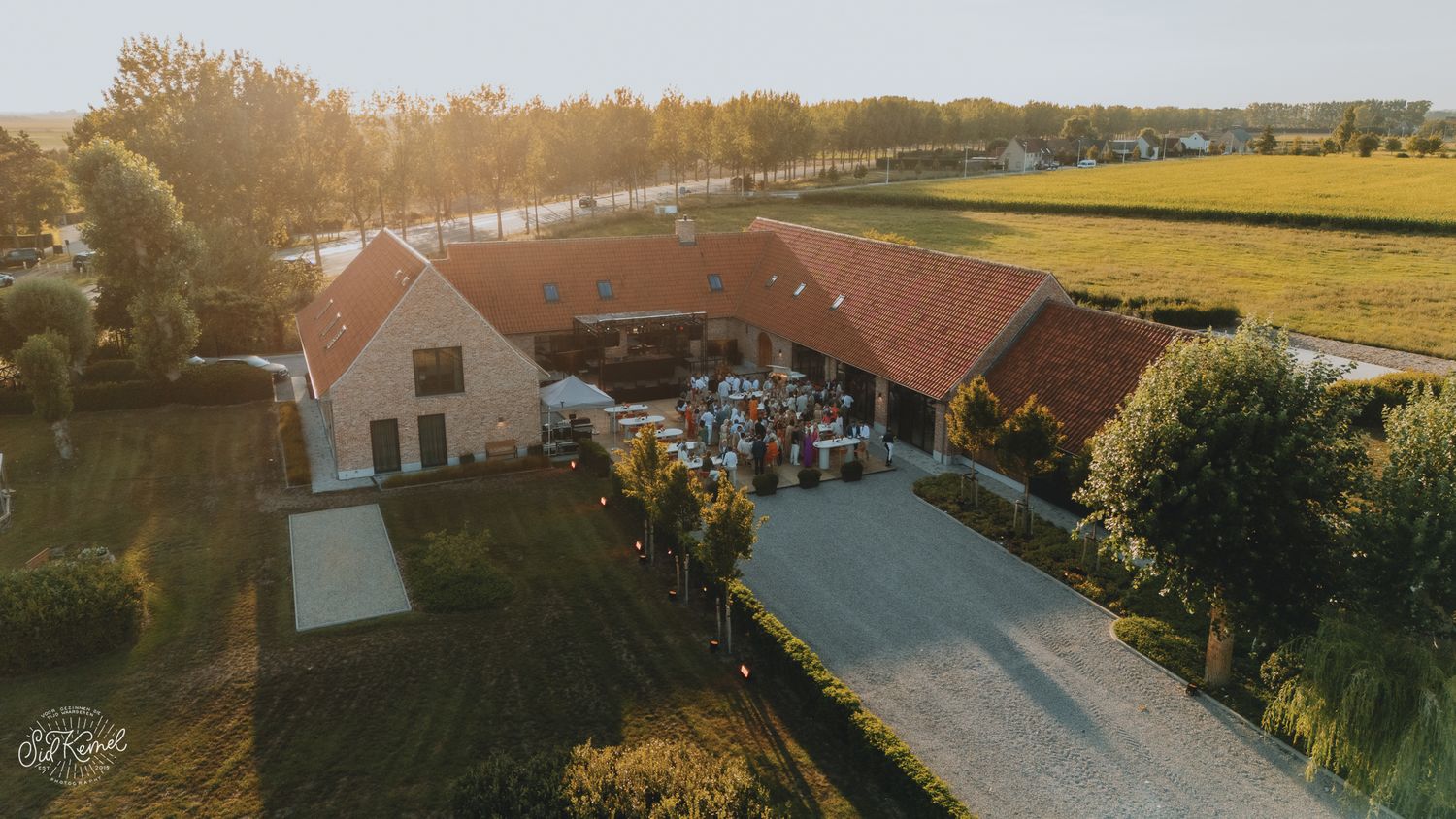 Aerial view of a rustic farm venue surrounded by golden fields at sunset during an event.