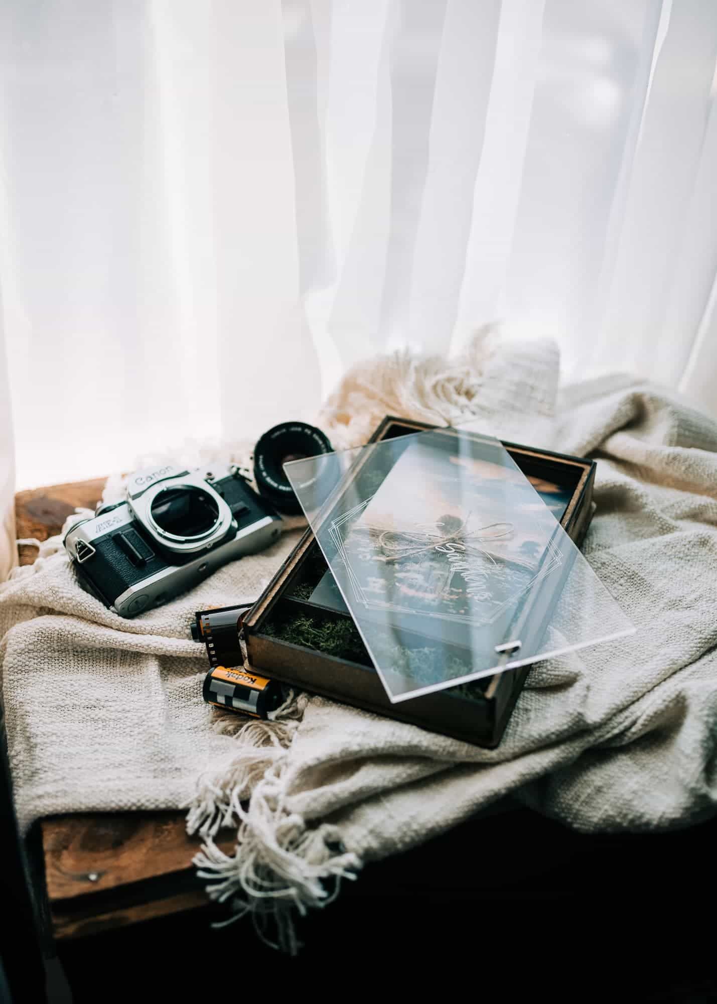 Een bed met een camera, een houten kistje met afdrukken er in, vastgelegd door Sid Kemel Photography