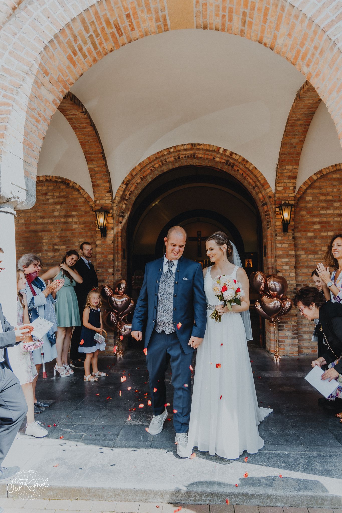 een zonet pas getrouwde koppel die aan de uitgang van de kerk elkaar kussen omring door familie en vrienden op een zonnige dag in Nieuwpoort