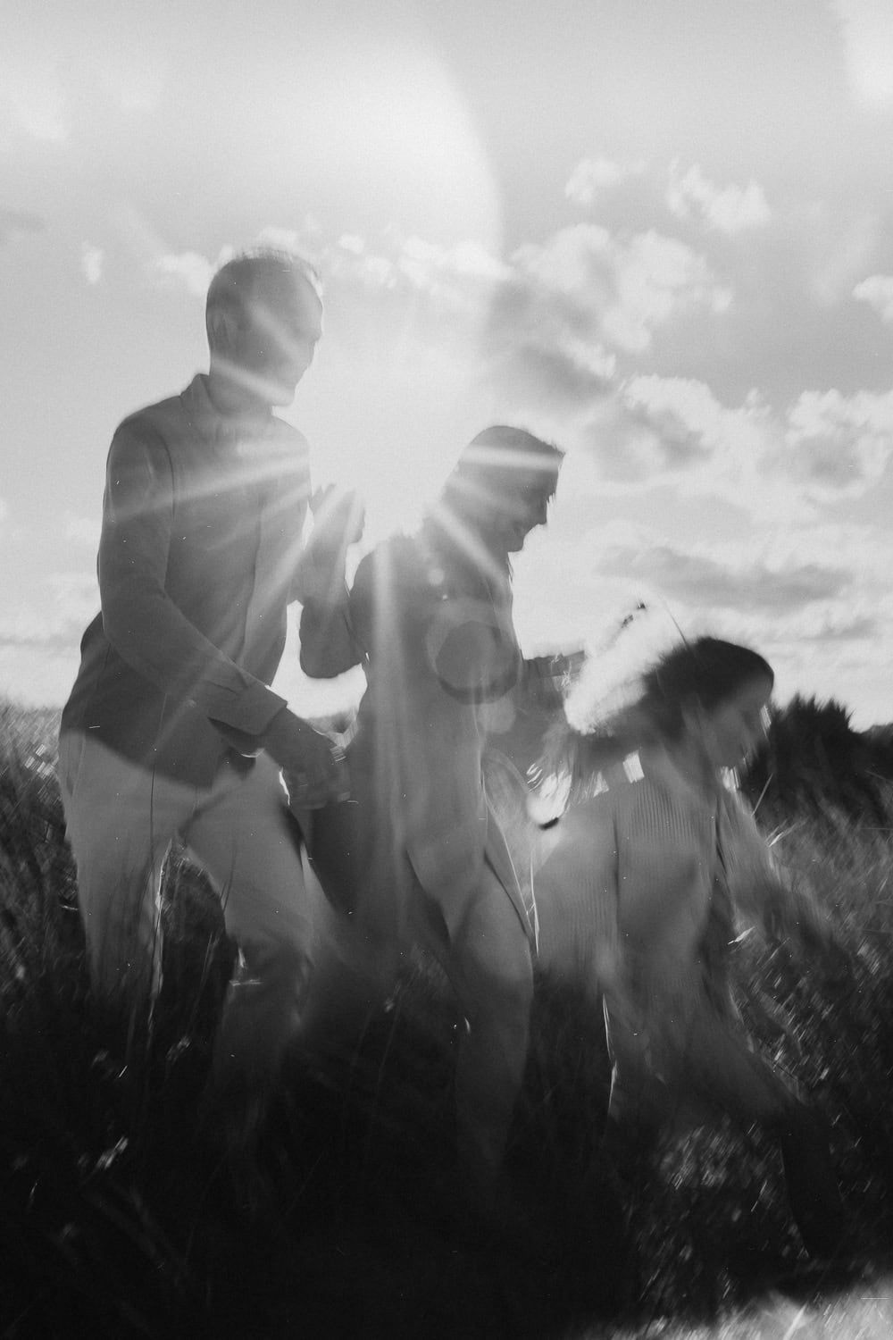 Zwart-witfoto van drie personen die hand in hand door het gras rennen. Zonlicht zorgt voor een dromerige en vrolijke sfeer.