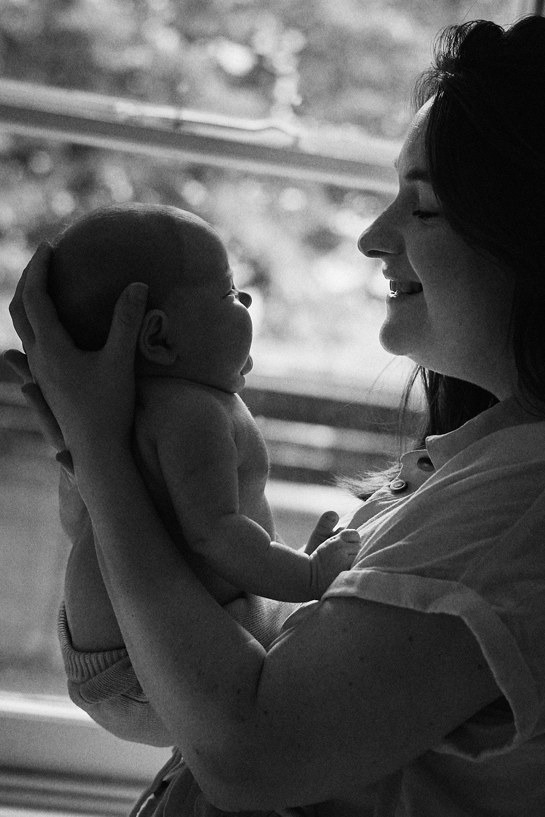 A tender black and white moment captured between a small infant and caregiver by a window.