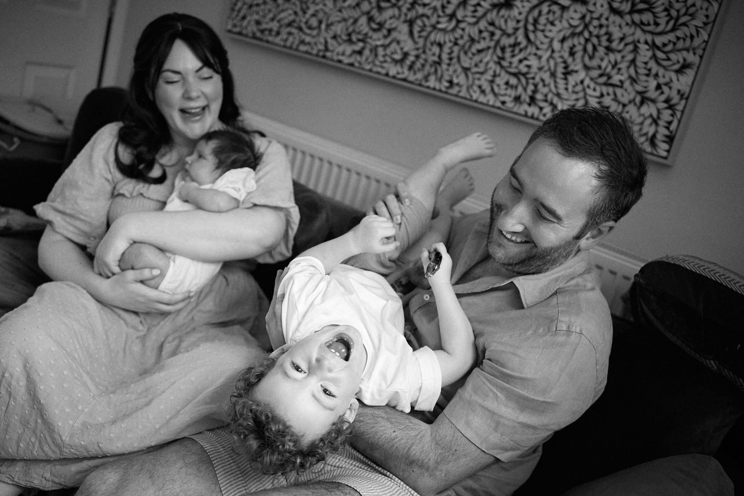 A candid black and white photo of a family sharing playful moments together on a bed.