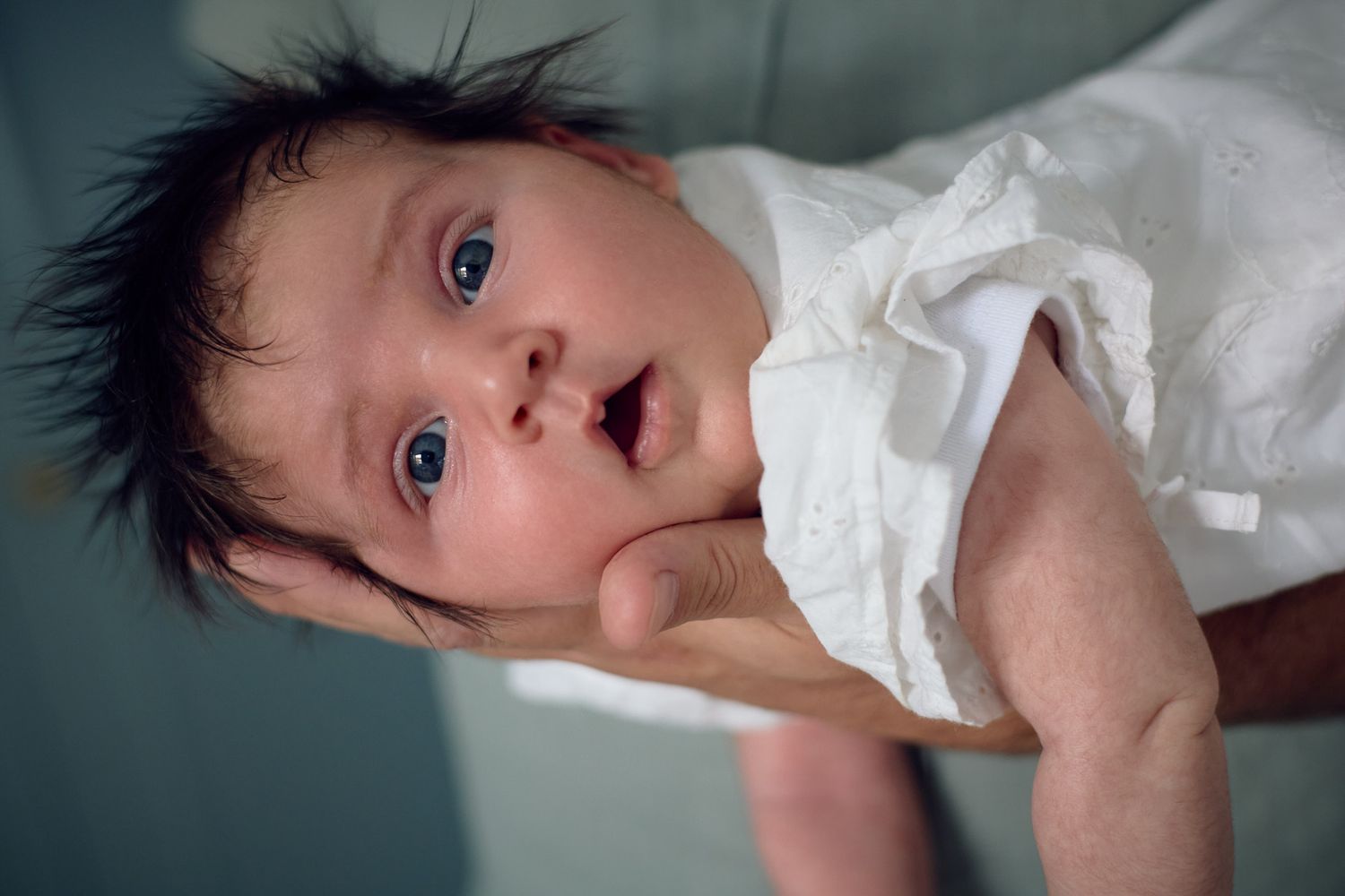 A baby in white clothing lies on their back with wide-eyed expression.