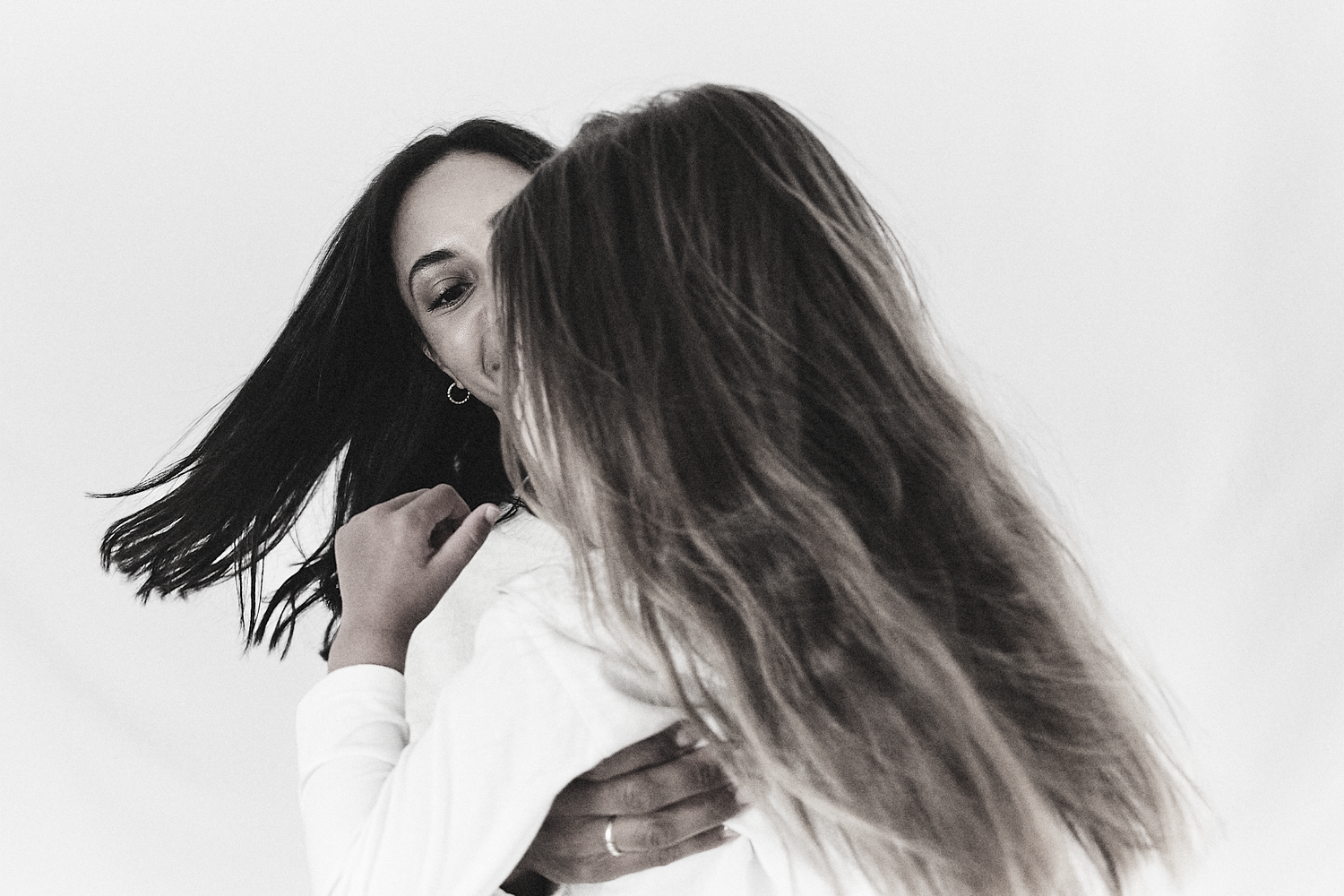 Black and white photo of two women embracing, with long hair flowing dramatically against a white background.