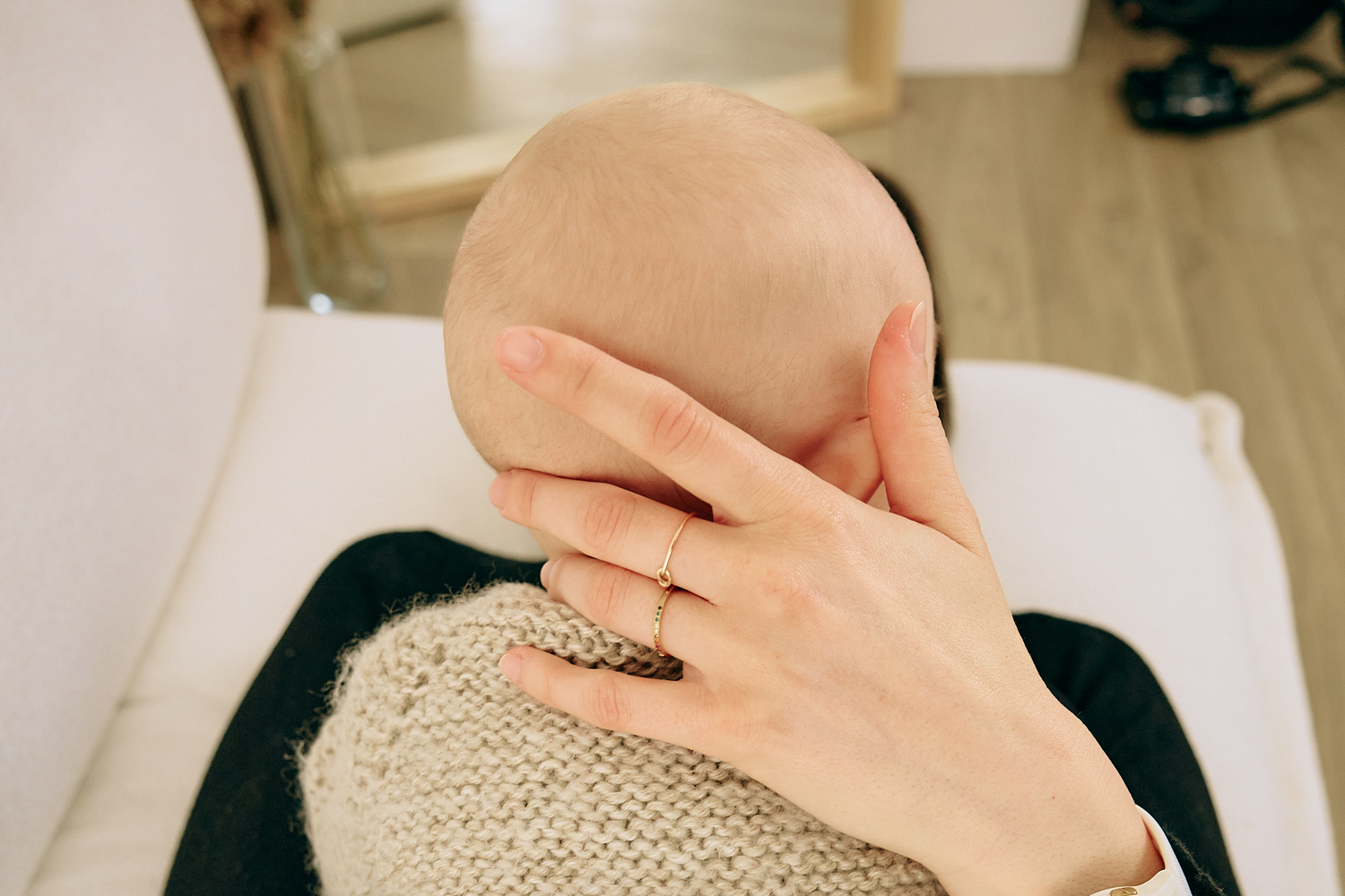 A parent tenderly cradling a newborn baby's head, wearing a gold ring, with the infant wrapped in a knit blanket.