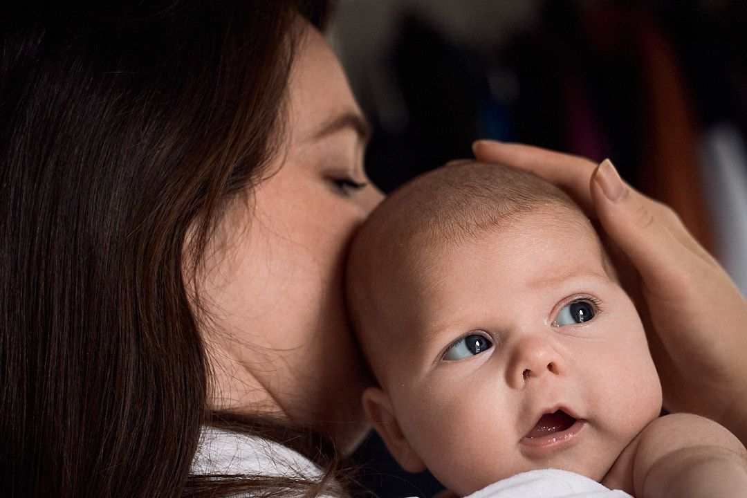 A gentle moment captured as a caregiver gives a baby a loving kiss on the head.
