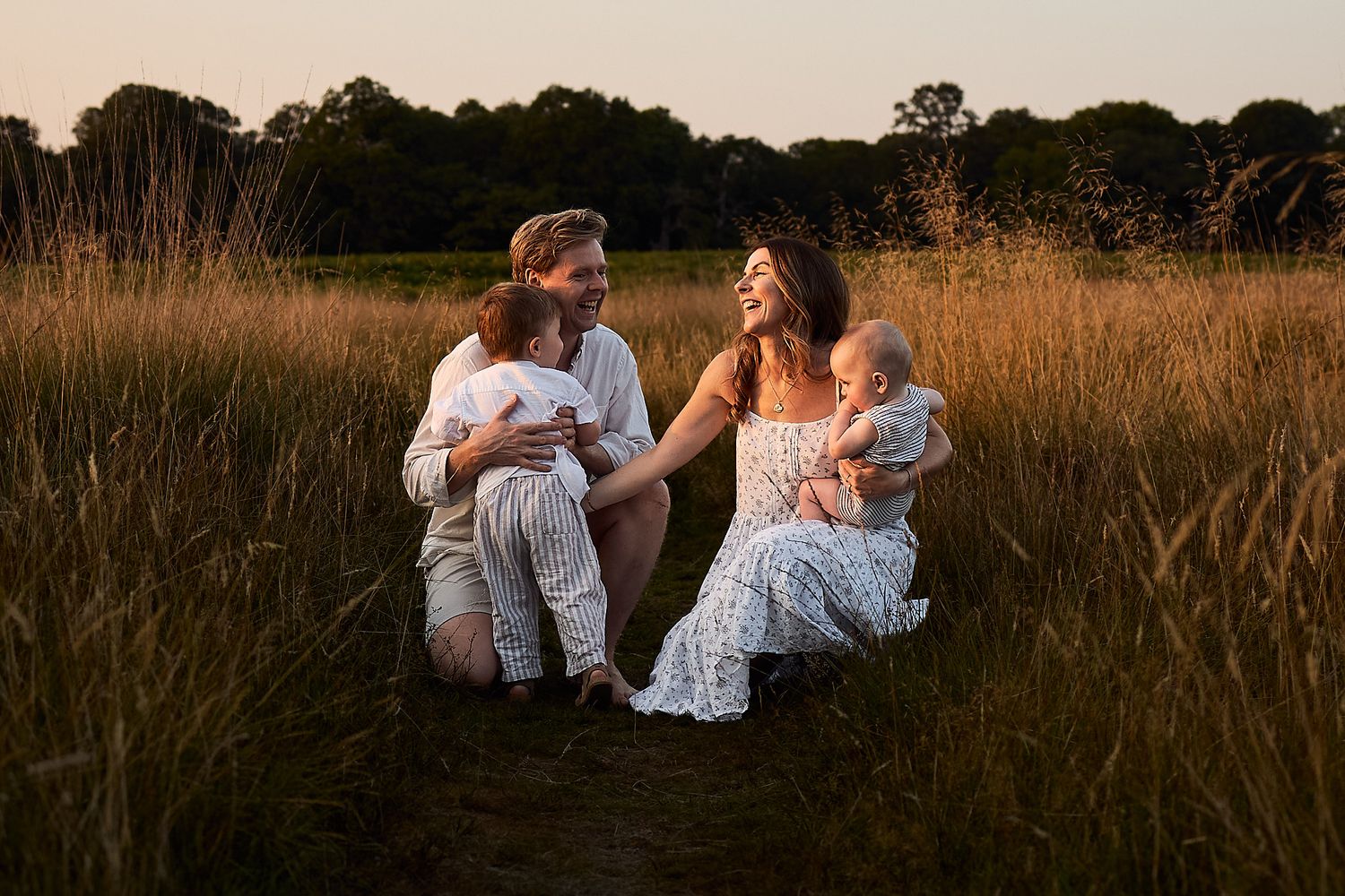 Family sitting together in tall grass during golden hour sunset photo session.