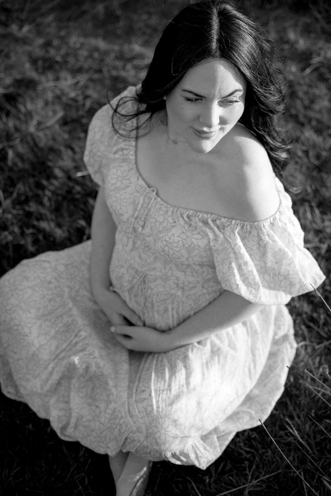 Black and white portrait of woman in lace dress sitting in field.