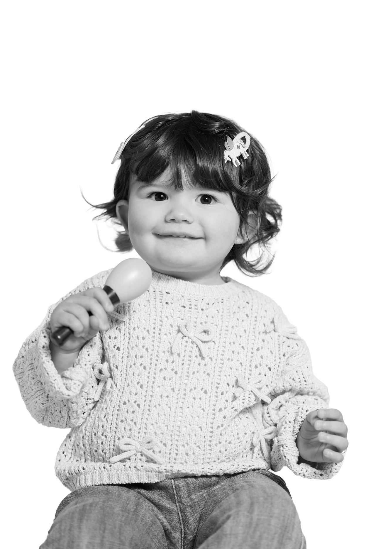 Black and white photo of a cute toddler girl in a knit sweater holding a toy microphone with a hair clip.